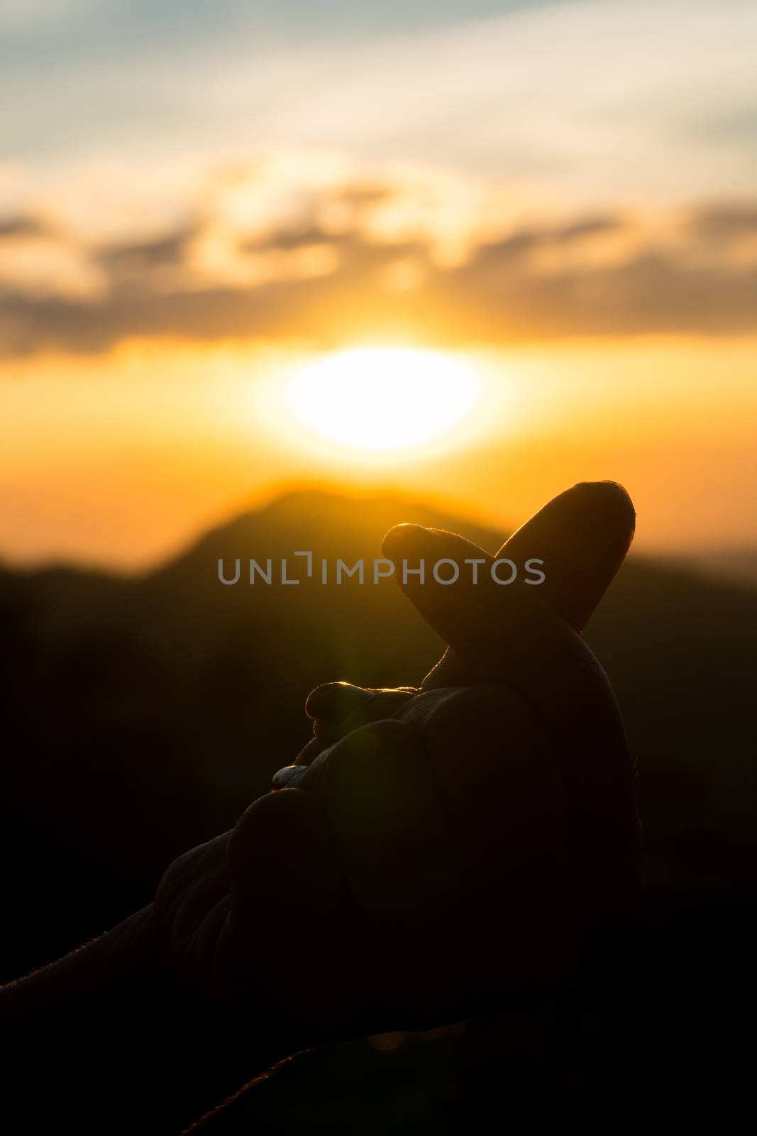 The hand of a woman showing a mini heart symbol on blur mountain at sunset background
