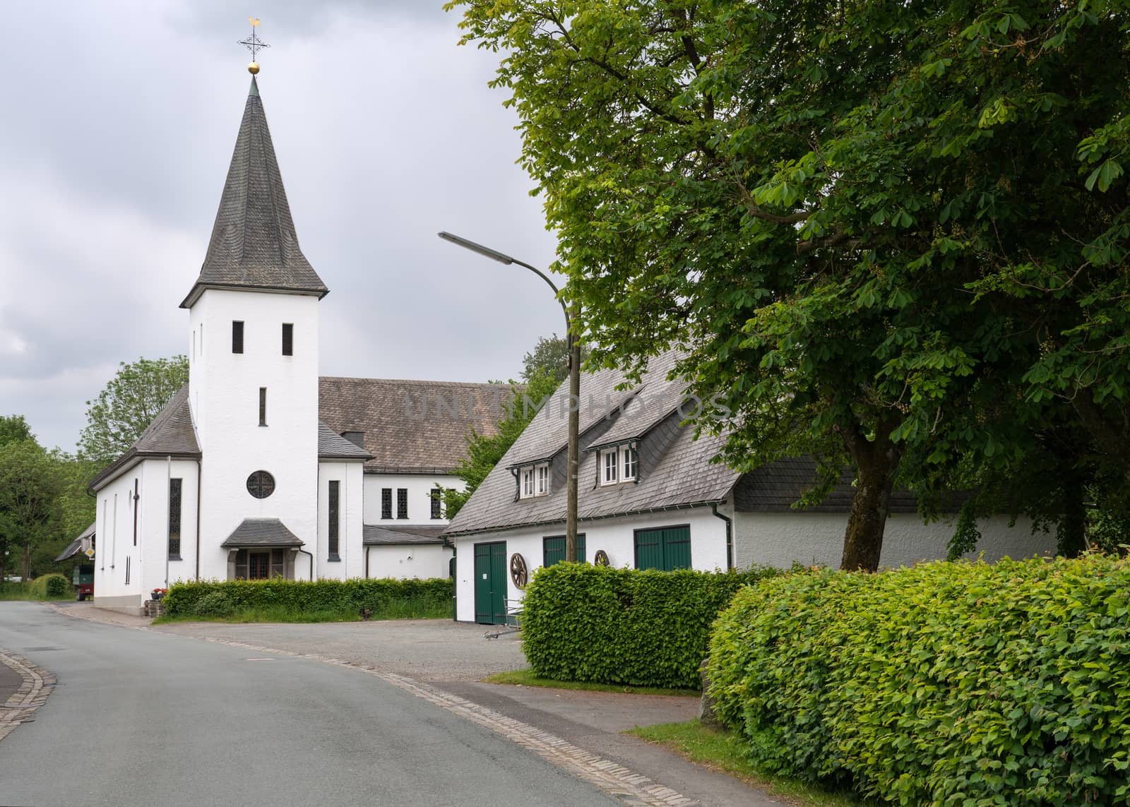 View along the central street of the Sauerland village Westfeld with parish church, old buildings and tree, Schmallenberg, Germany