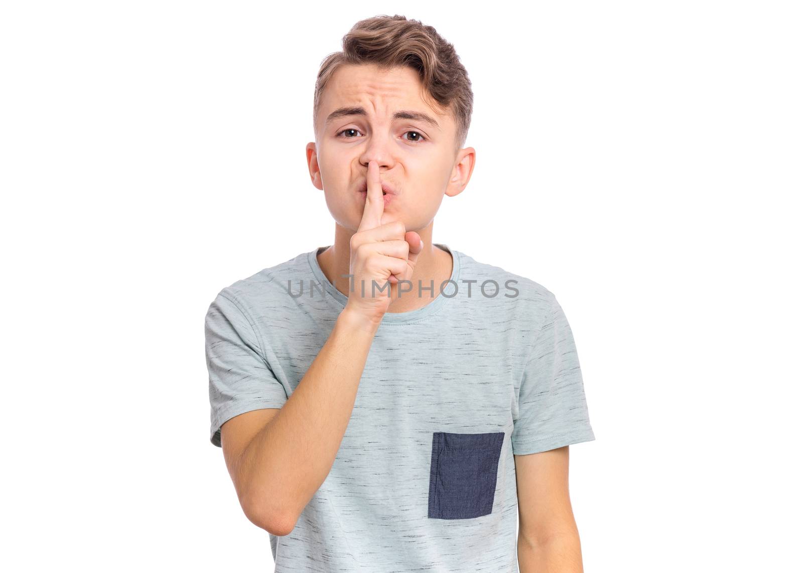 Handsome teen boy keeps fore finger on lips, asking for silence, isolated on white background
