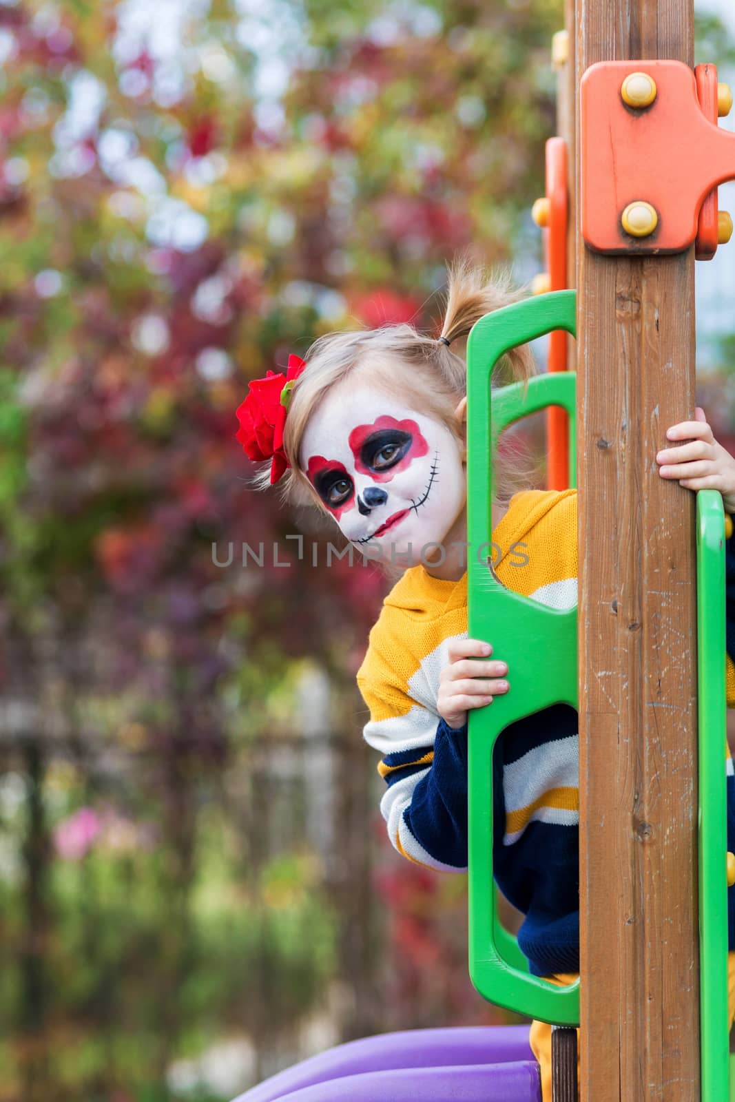 A little girl with Painted Face, climbed the slide on Day of the Dead. by galinasharapova