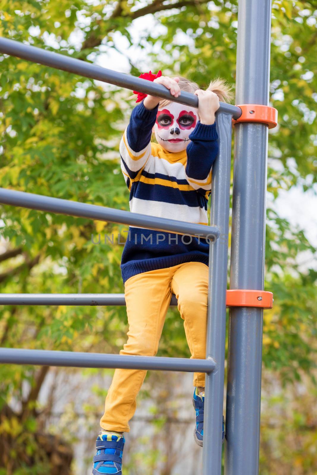 A little preschool girl with Painted Face, climbed the Swedish wall in the playground, celebrates Halloween or Mexican Day of the Dead.