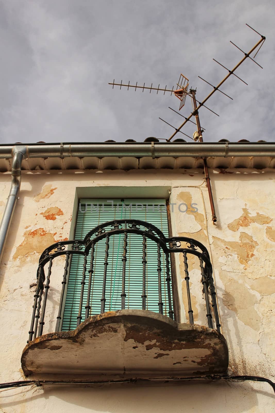 Old house facade with rusty balcony and green blind next to television antenna . Alcaraz village, Castilla La Mancha, Spain.