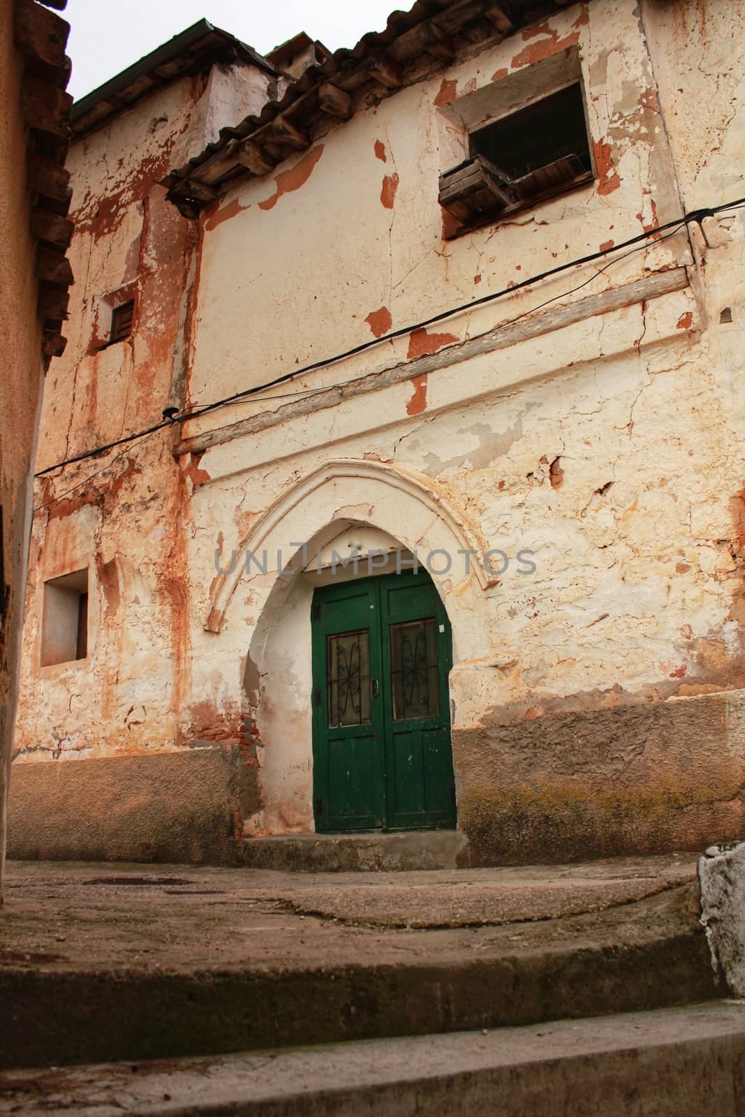Old abandoned house facade with green wooden door in Alcaraz, Spain
