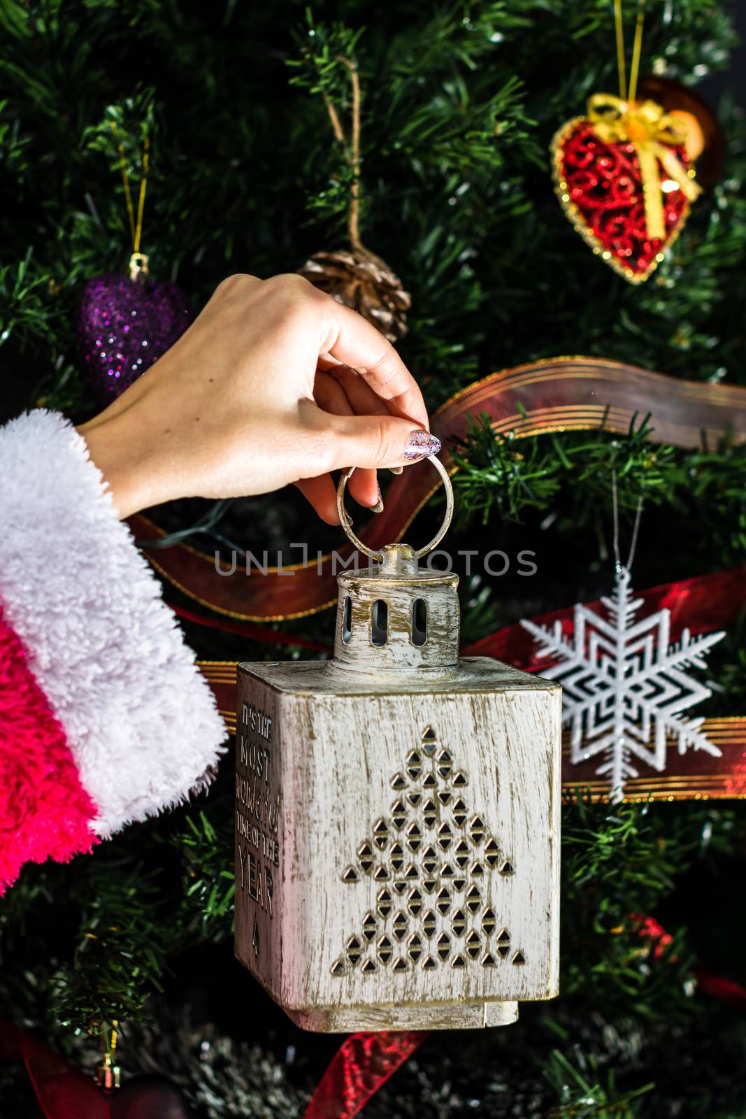 Hands holding Christmas ornament in front of Christmas tree. Decorating fir branches with Christmas decorations.