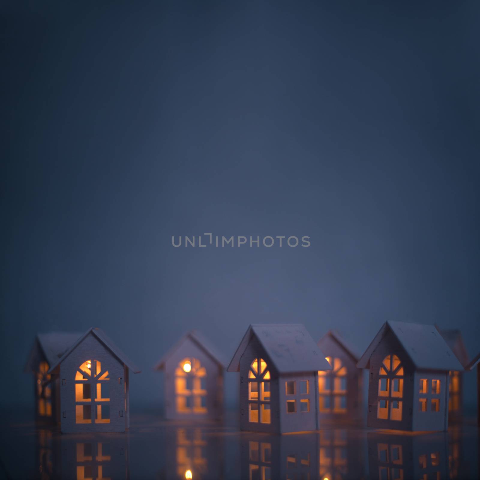 Christmas card of small glowing toy houses over dark blue background with copy space for text