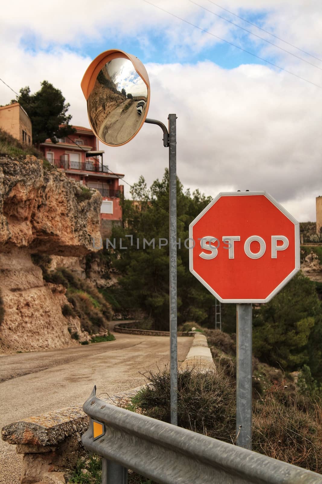 Stop sign and mirror panel on mountain road in a cloudy day. Road surrounded by vegetation.