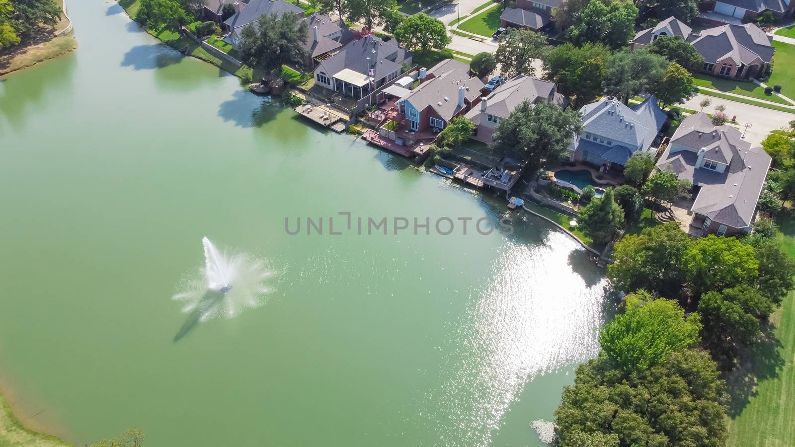 Top view upscale lakeside houses with water fountain in Flower Mound, Texas, America. Row of two story waterfront homes with private docking, swimming pools. Wealthy residential area