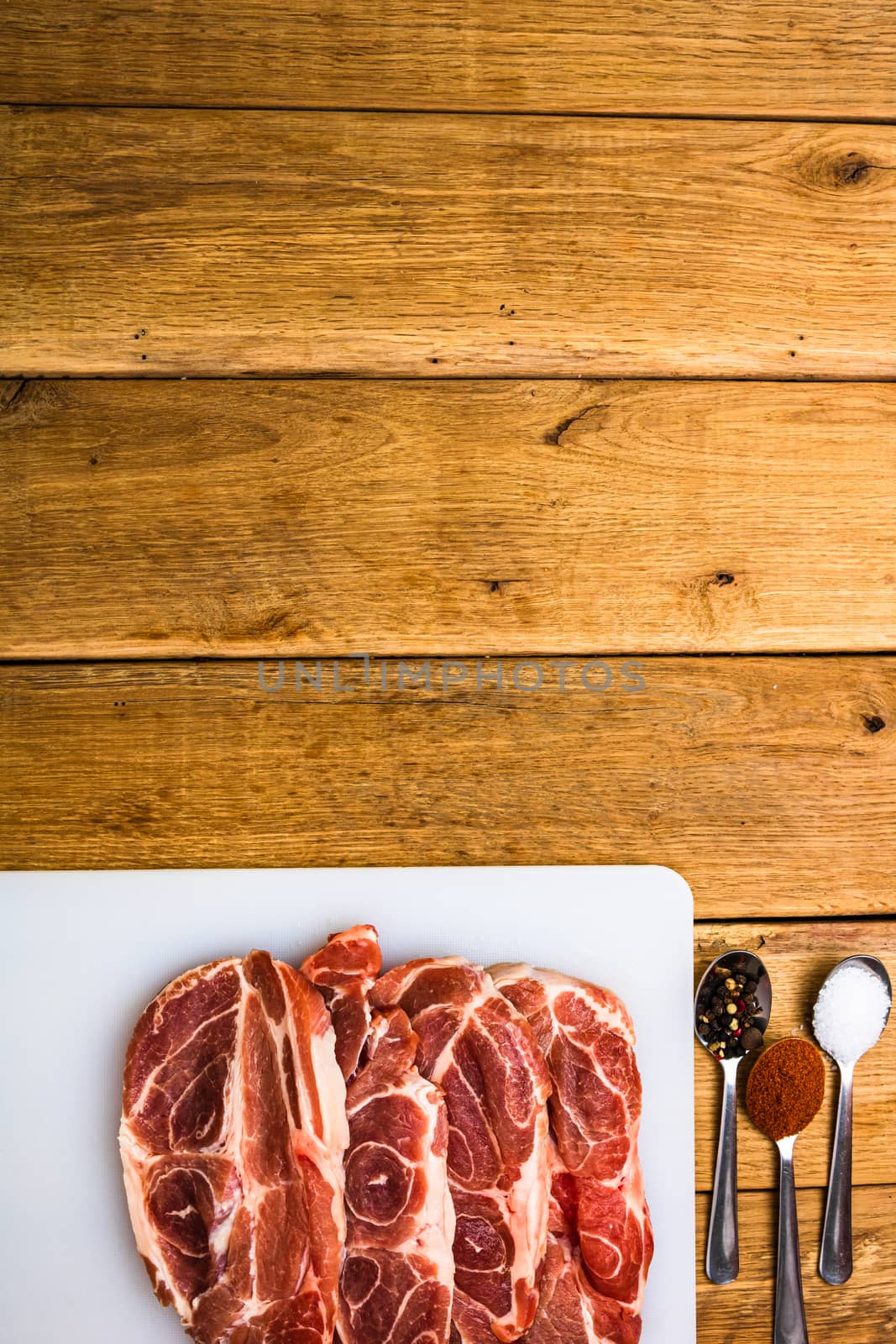 Pork chops with condiments on a white cutting board over wooden table, meat for bbq, top view, copy space, barbeque concept