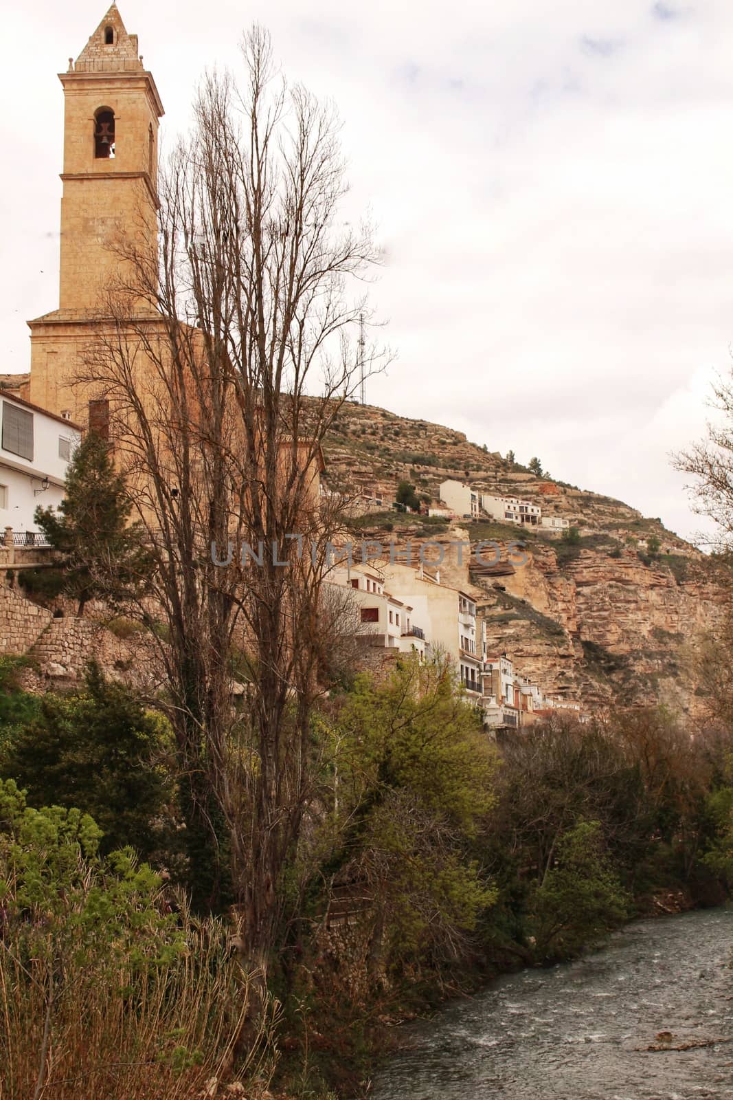 Beautiful overview of the town of Alcala de Jucar with the fortress castle and the church in spring under gray sky