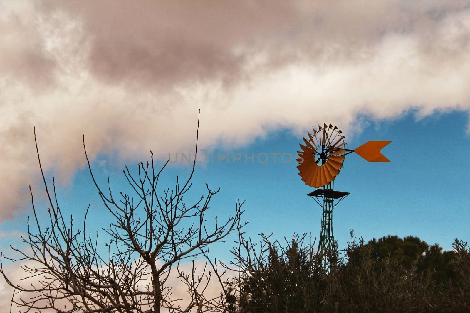 Yellow Windmill with tale vane under cloudy and windy weather in the countryside