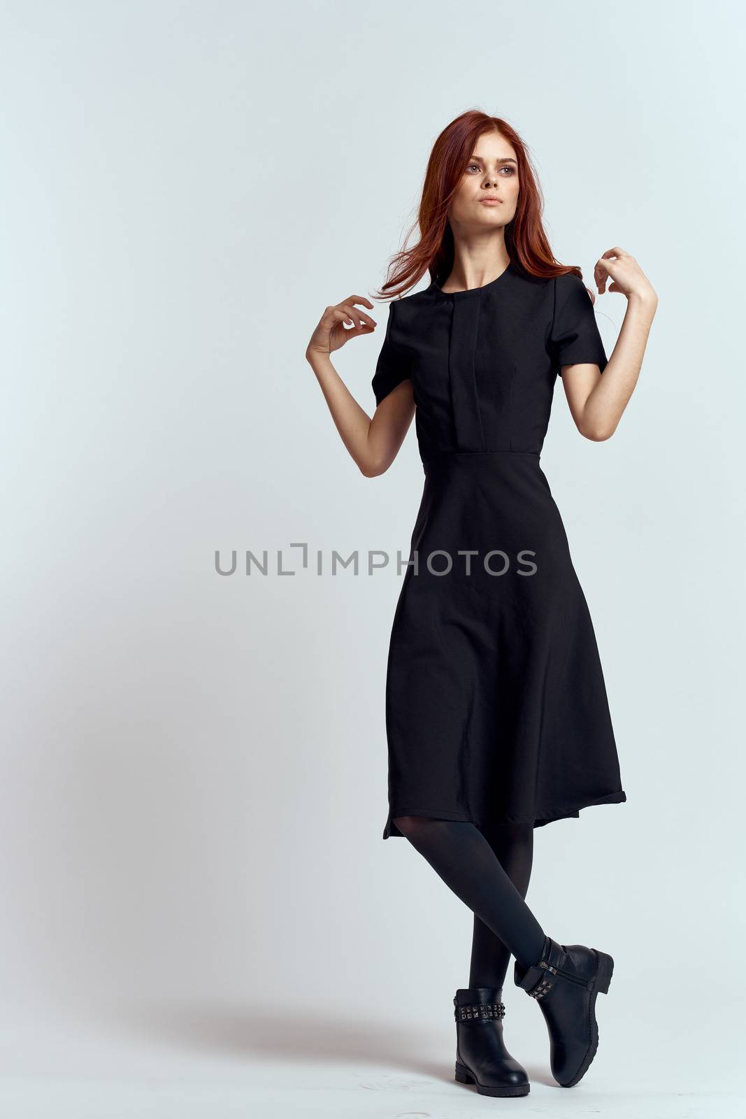 A woman in a black dress on a light background and pantyhose shoes red hair and pose in full growth by SHOTPRIME
