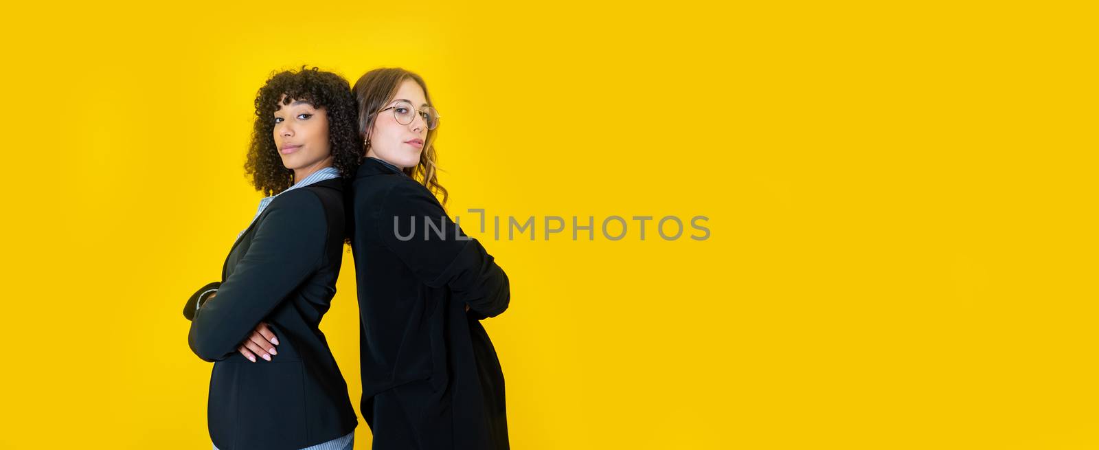 Two business women black Hispanic and Caucasian looking at the camera with a confident expression on big yellow copy space - Optimistic working people in office clothes collaborating by robbyfontanesi