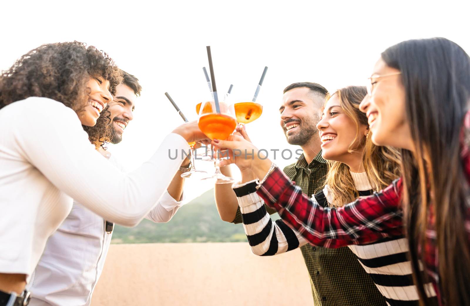 Mixed race happy friends group toasting with spritz glasses outdoor at sunset - Young people having fun together drinking cocktail for aperitif time - Bright vivid filter with focus on bearded men by robbyfontanesi