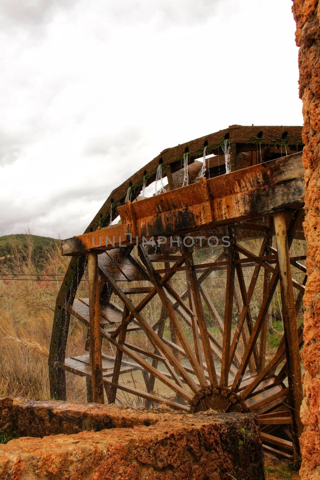 Old wooden Waterwheel and Cabriel River on its way through Casas del Rio village, Albacete, Spain. Landscape between cane field and mountains.