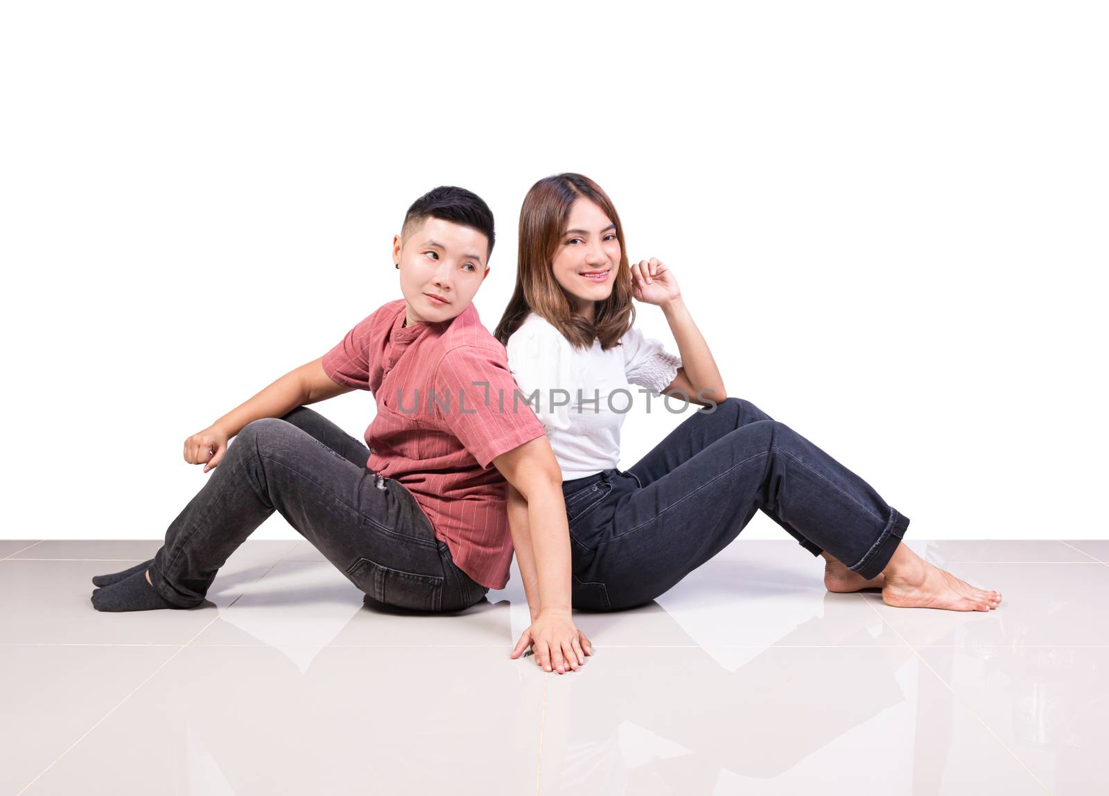 Two smiling woman young girls and happiness tomboy friends sitting back to back hold hand on tile floor in home with white background