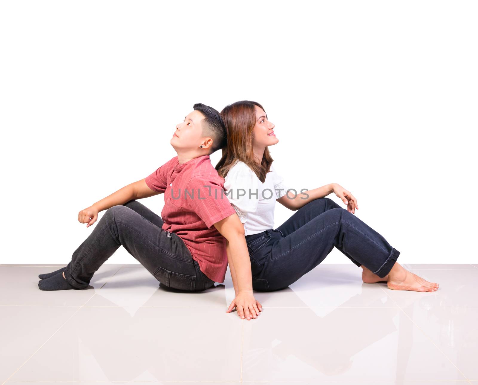 Two smiling woman young girls and happiness tomboy friends sitting back to back hold hand on tile floor in home with white background