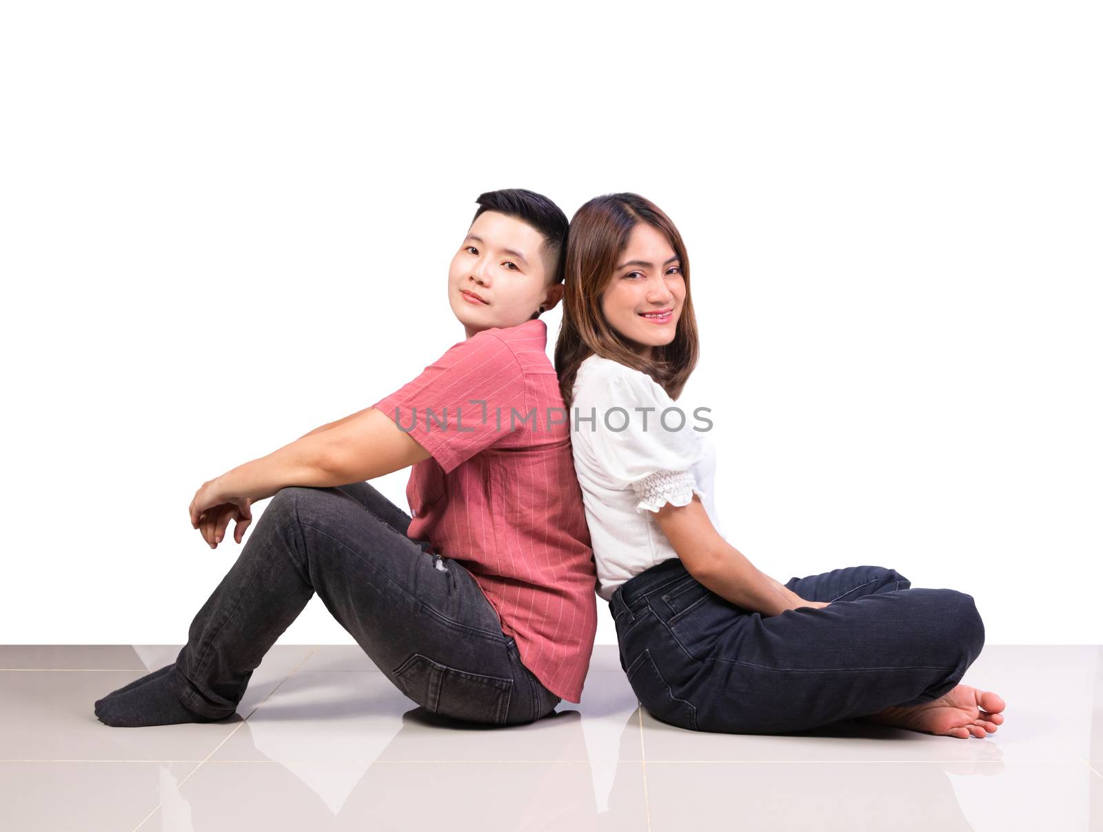 Two smiling woman young girls and happiness tomboy friends sitting back to back on tile floor in home with white background