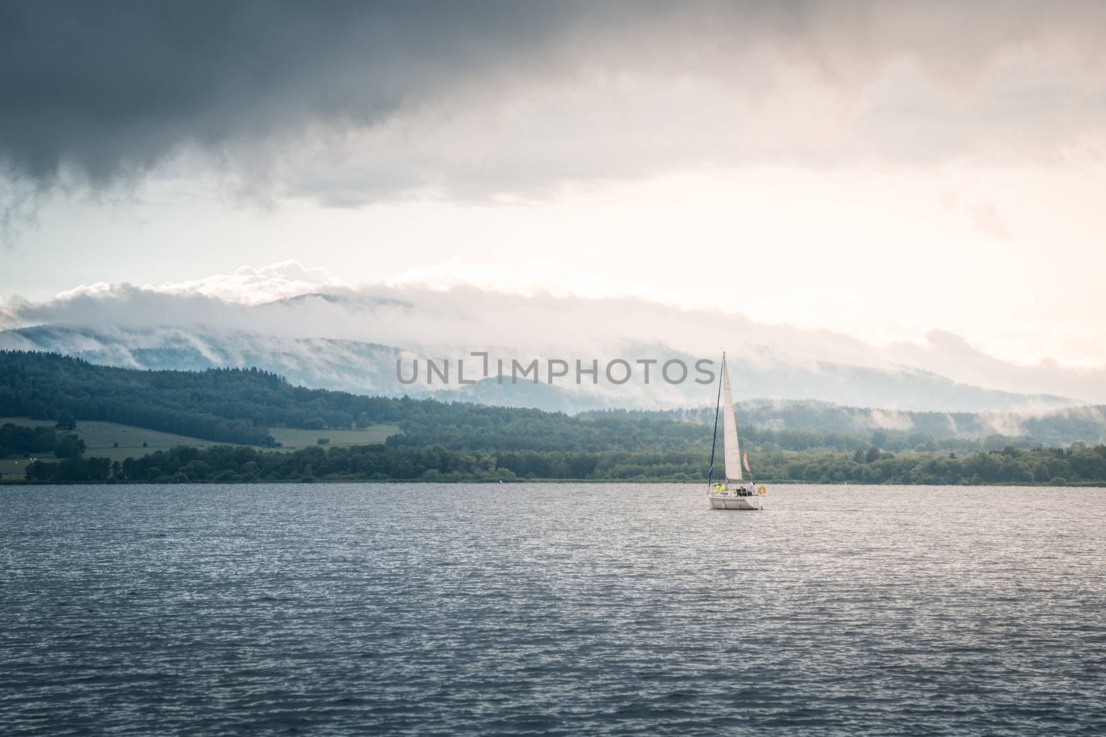 Sailing boat floats on the lake with stormy clouds sky. Autumn sailboat ship water sport scene from Lipno