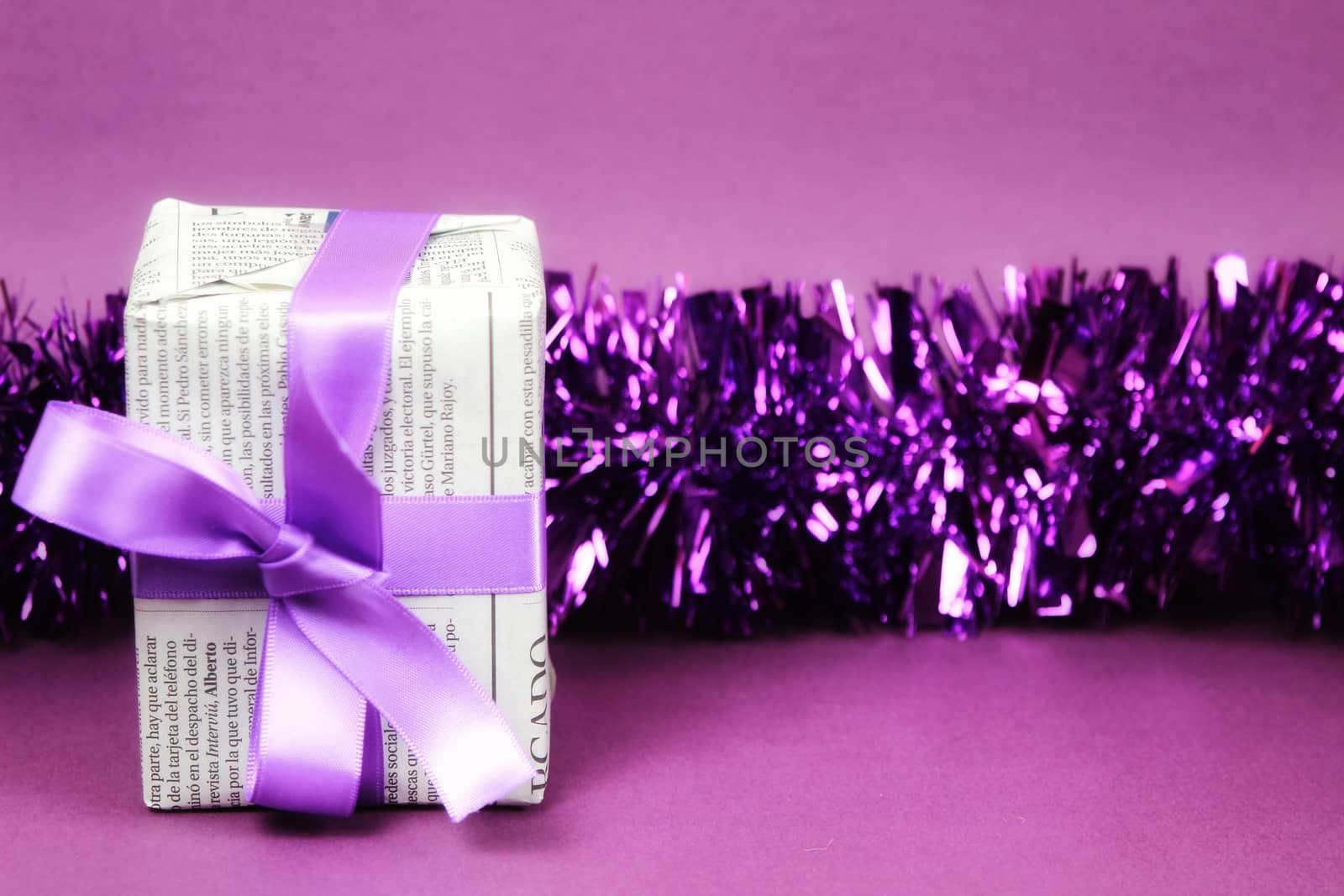 Gifts wrapped in old newspaper with purple bow, tinsel and rope on purple background