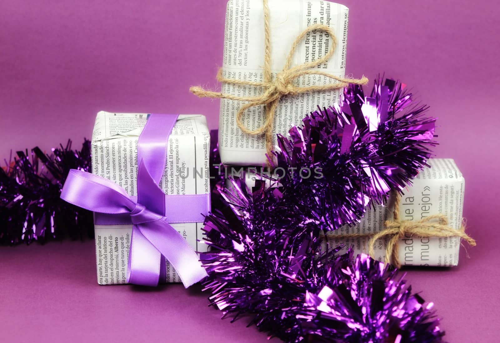 Gifts wrapped in old newspaper with purple bow, tinsel and rope on purple background