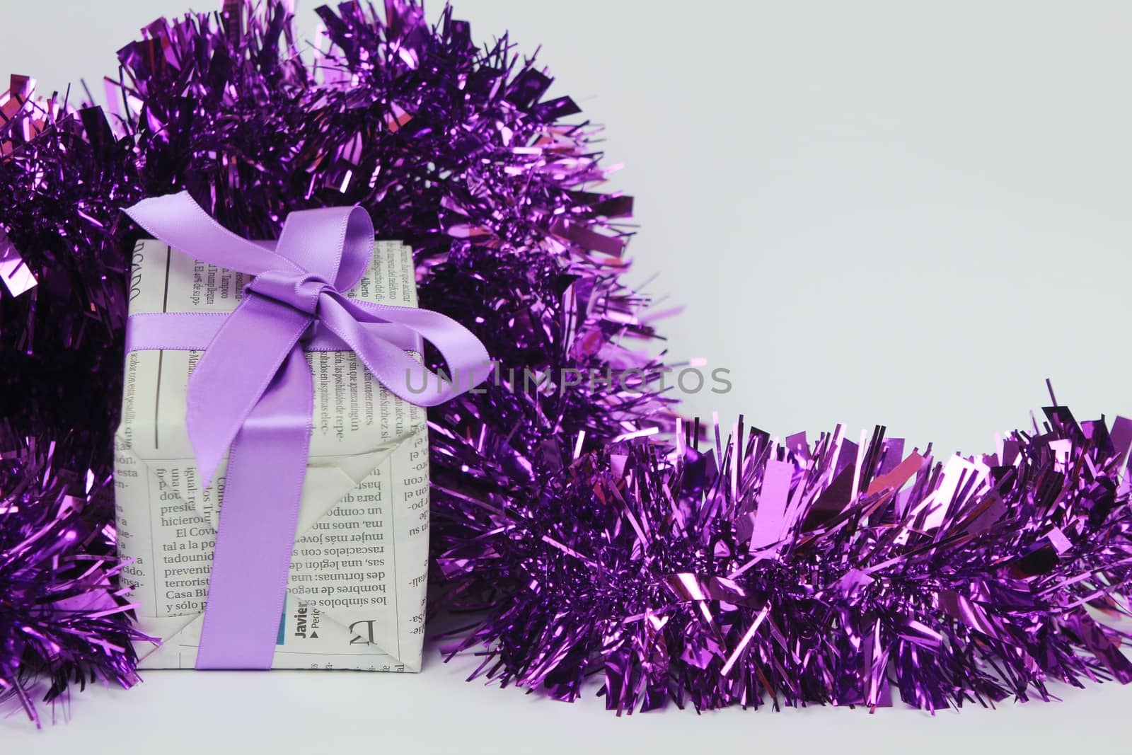 Gifts wrapped in old newspaper with purple bow and tinsel on white background