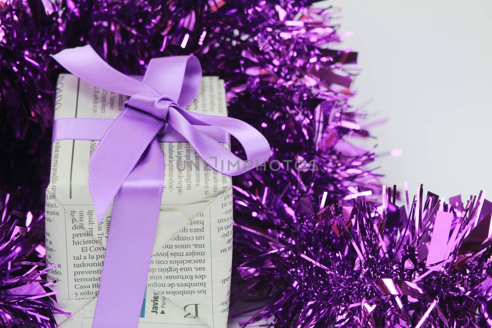 Gifts wrapped in old newspaper with purple bow and tinsel on white background