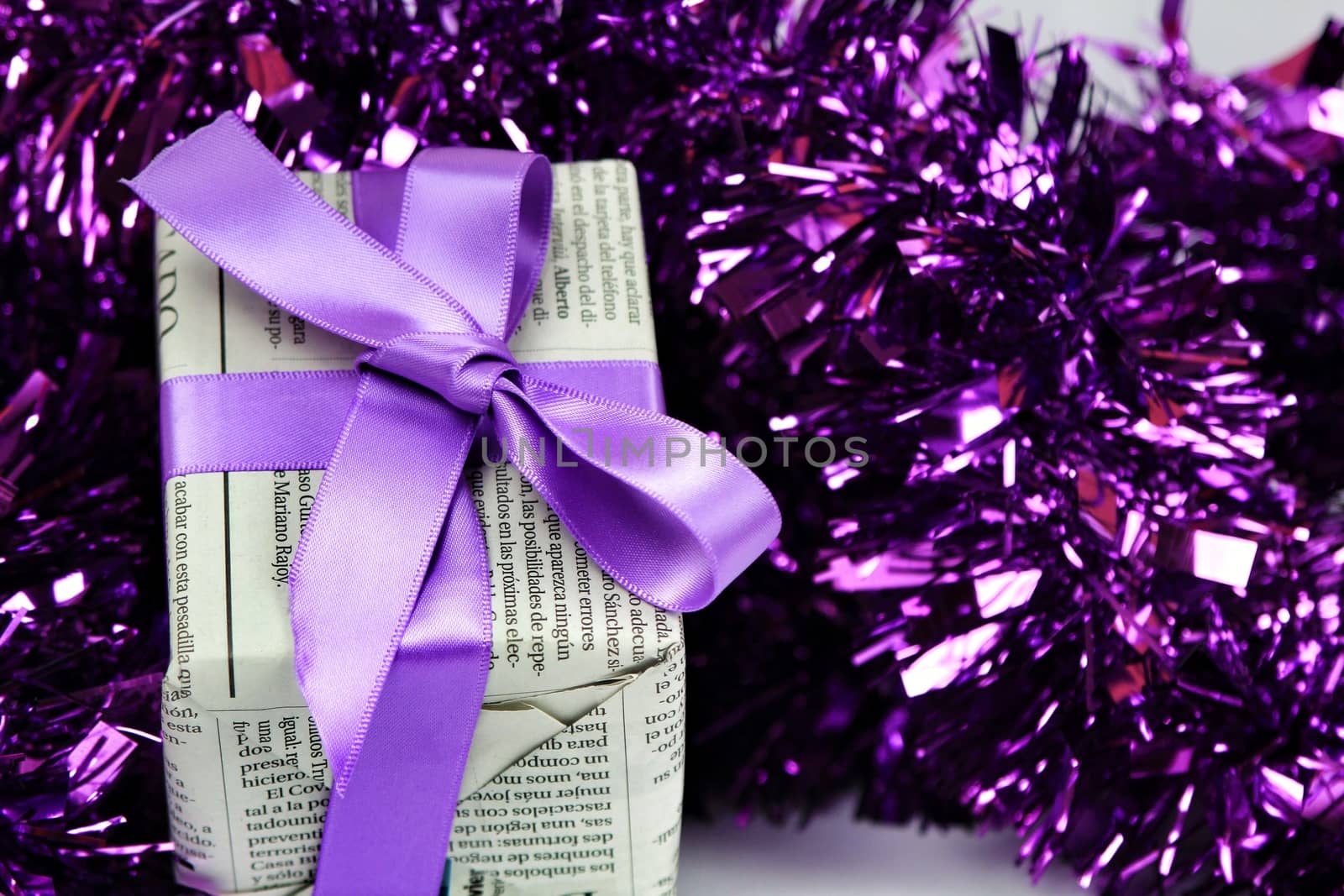 Gifts wrapped in old newspaper with purple bow and tinsel on white background