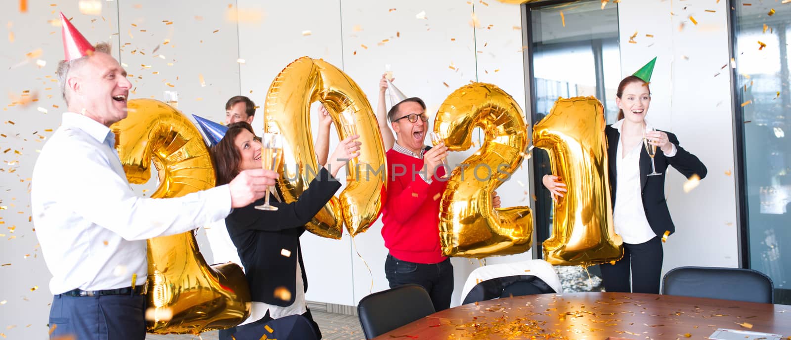 Business people are celebrating holiday in modern office drinking champagne and having fun in coworking. Merry Christmas and Happy New Year 2021. Balloon numbers