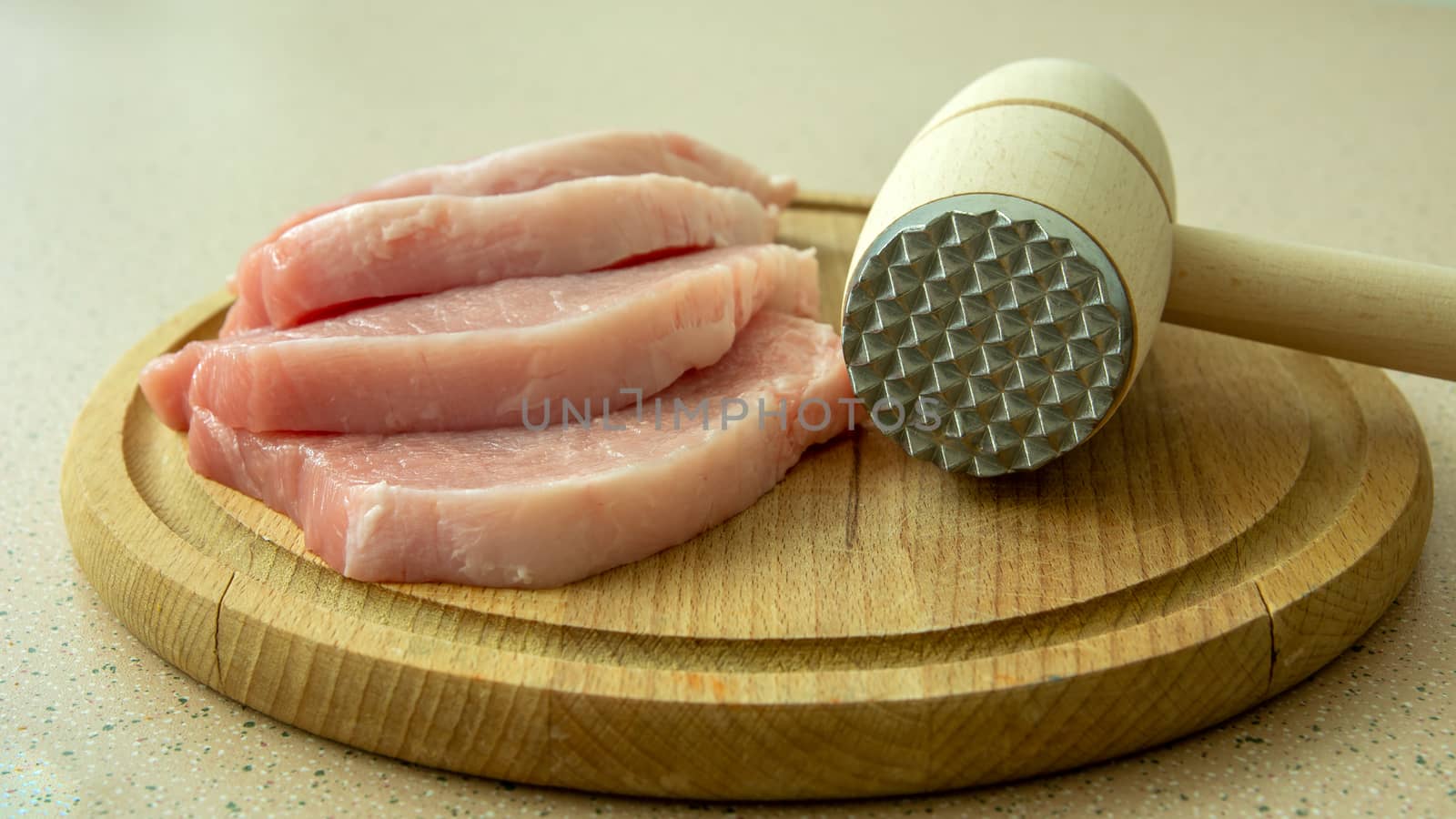 Raw pieces of loin on a wooden board and a meat mallet