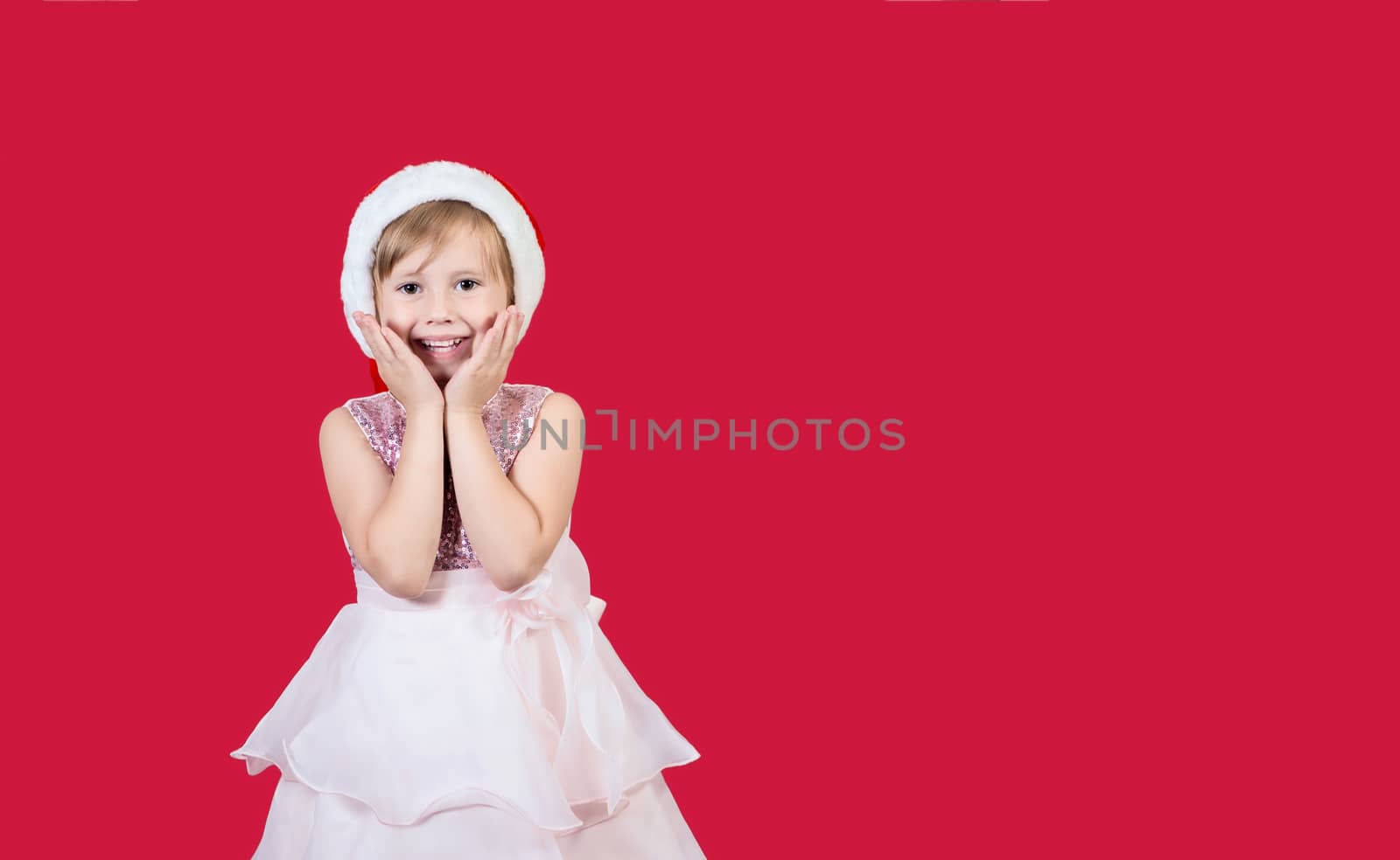 Surprised funny cacusian cute child girl in santa hat looking at the camera waiting for presents celebrating happy 2021 New Year isolated on red background. Merry Christmas presents shopping sale.