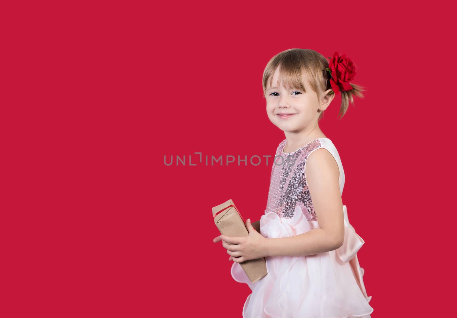 Beautiful cute cacusian little girl in an elegant dress and with a rose pin in her hair holding a gift and smiling. Merry Christmas or Valentine's Day presents shopping sale.
