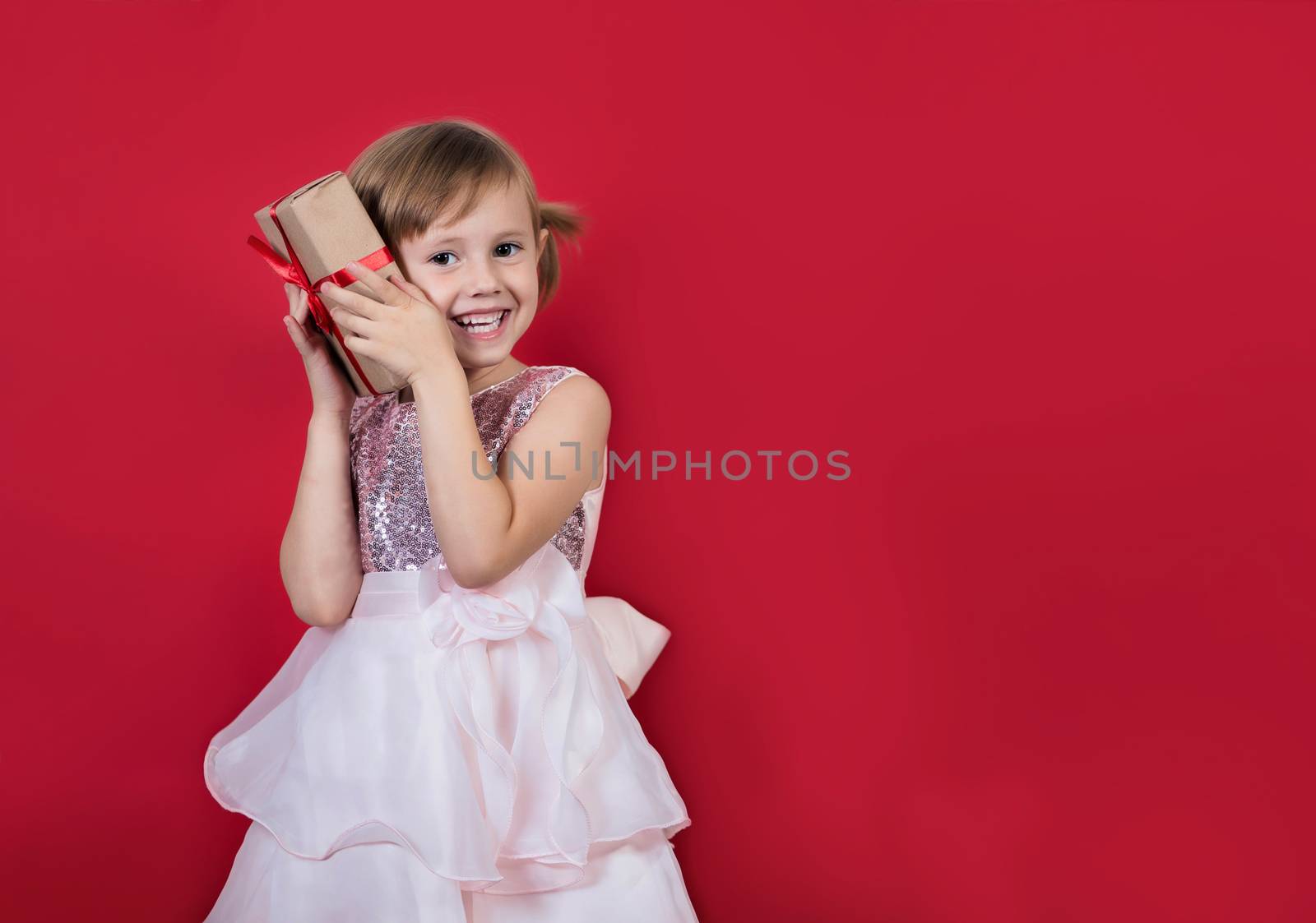 Cute adorable smiling girl holding christmas gift isolated on red by galinasharapova