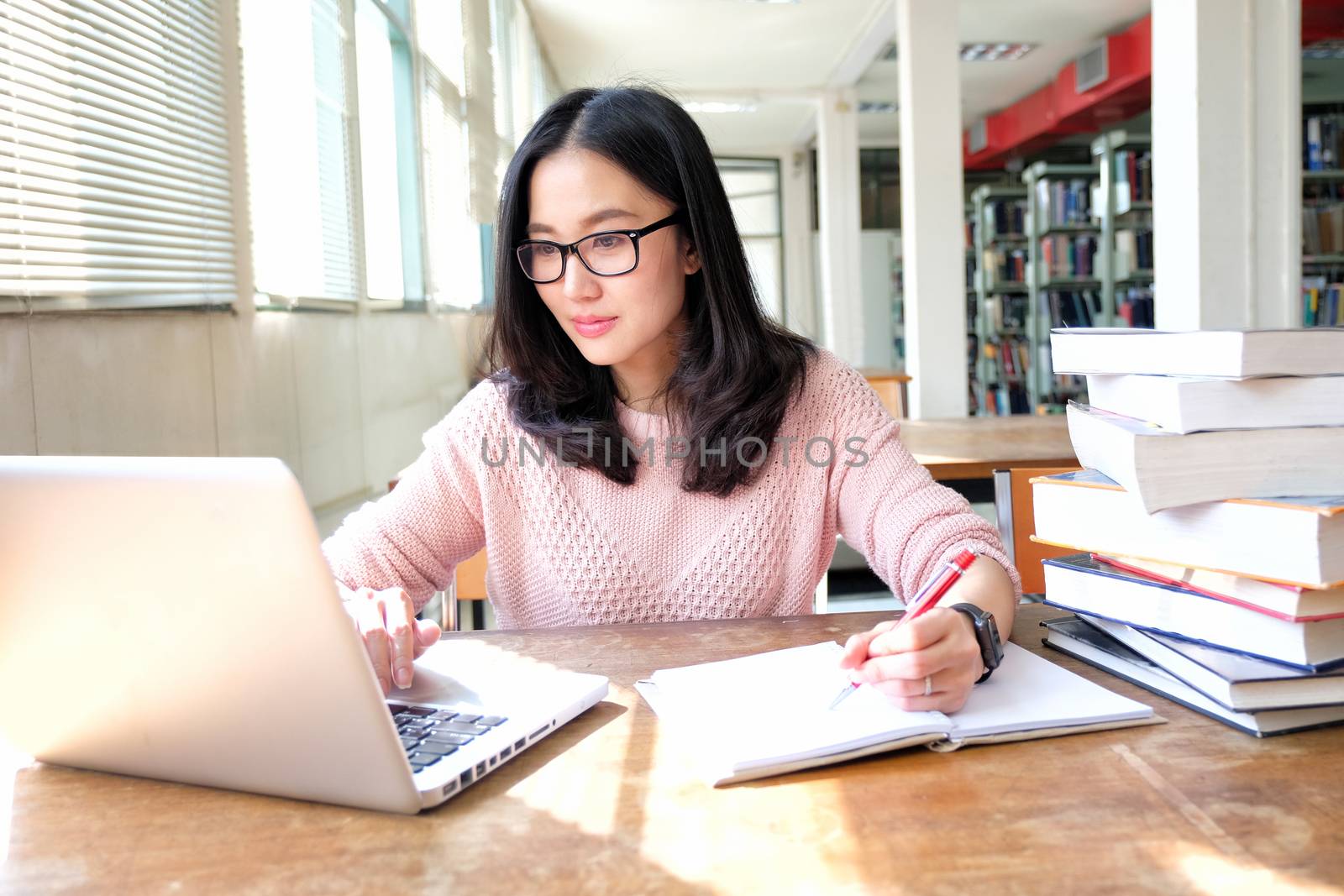 Young woman taking note and using laptop while studying in libra by Surasak