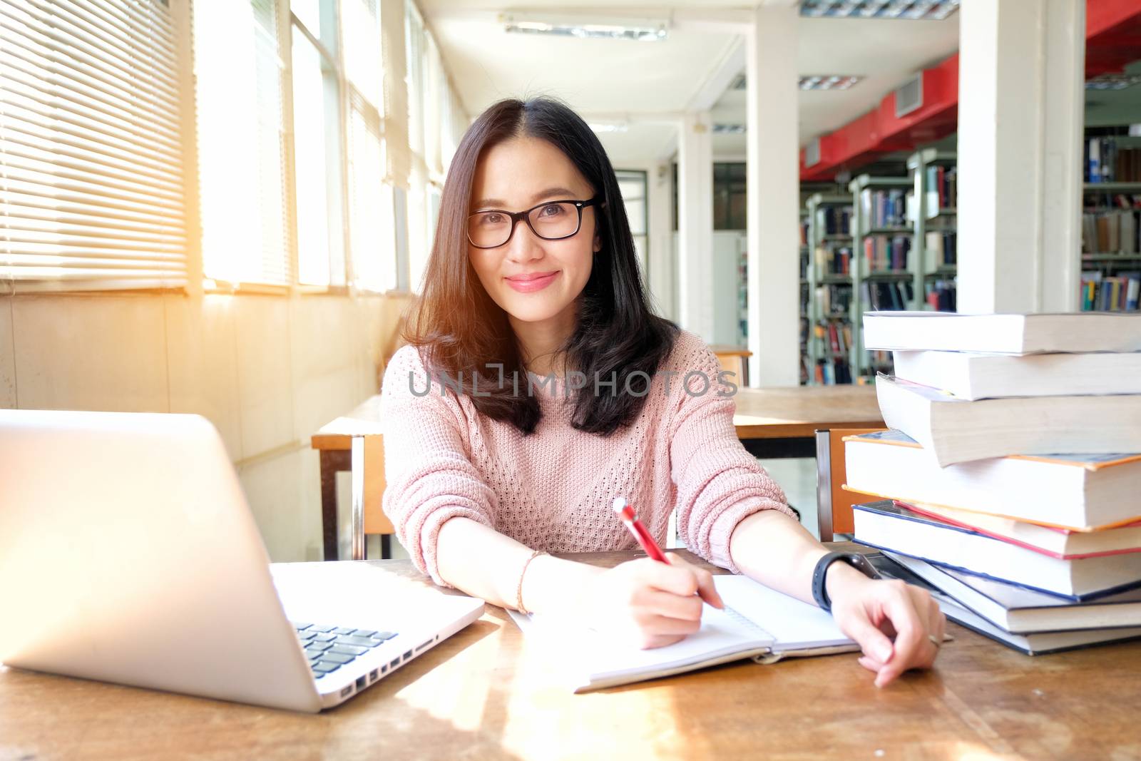 Young woman taking note and using laptop while studying in library