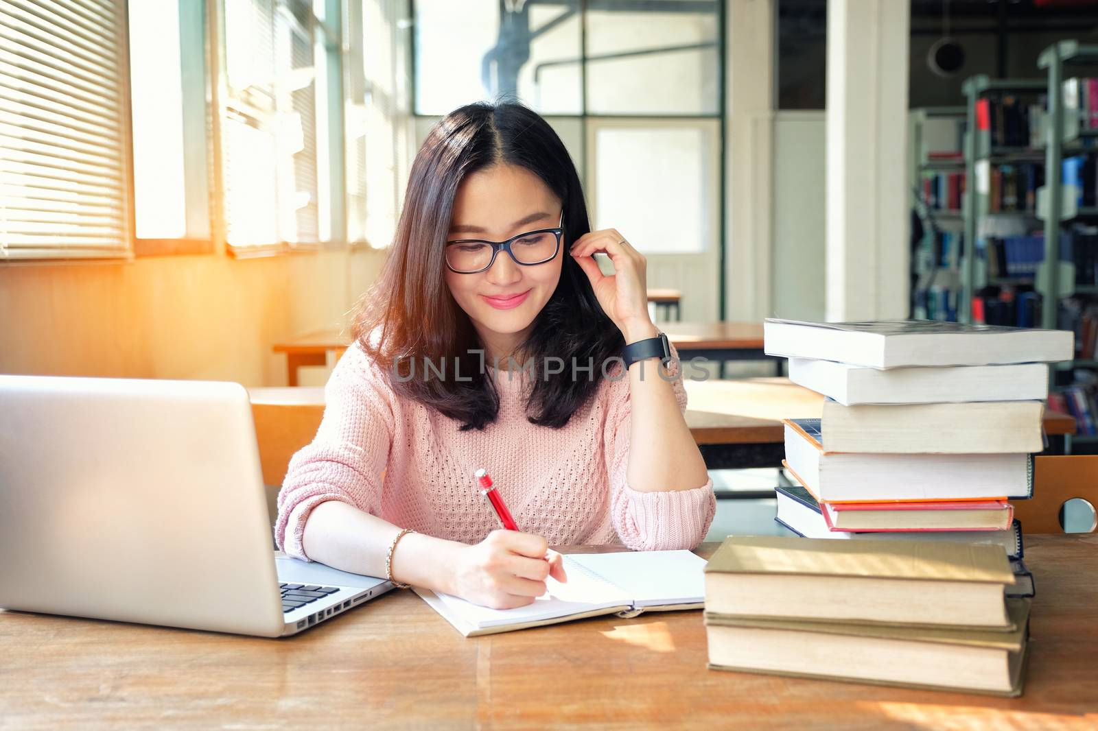 Young woman taking note and using laptop while studying in libra by Surasak