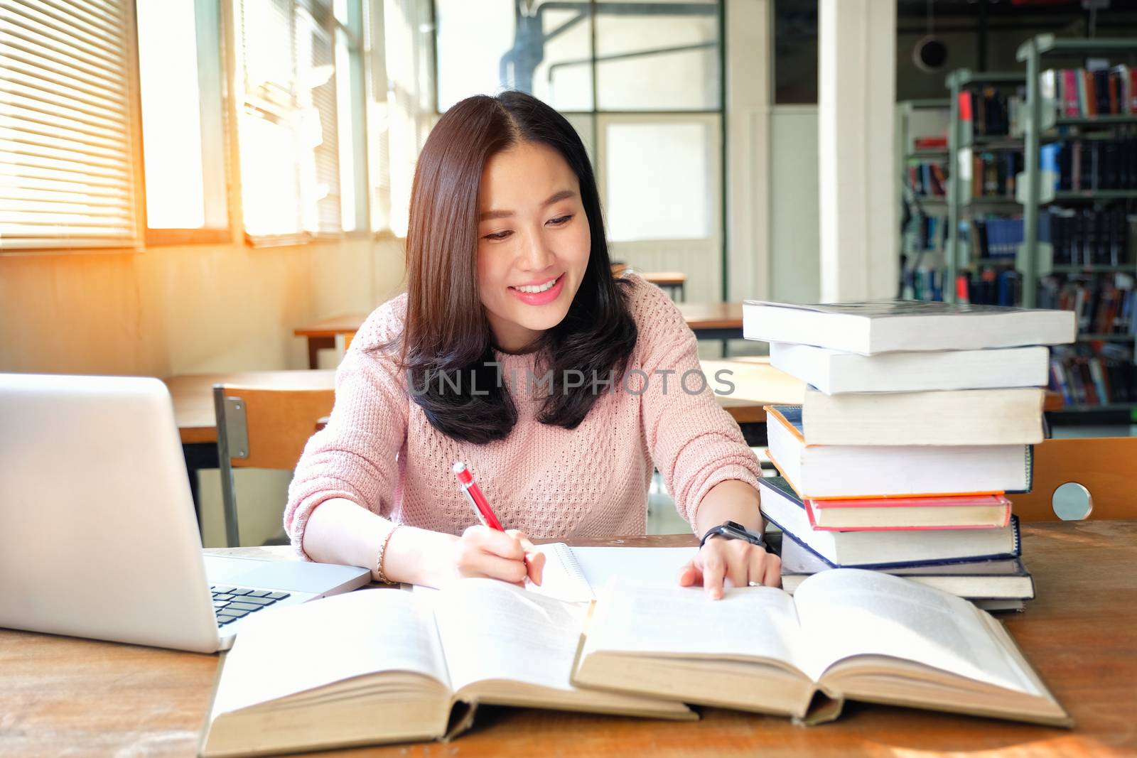 Young woman taking note and using laptop while studying in libra by Surasak