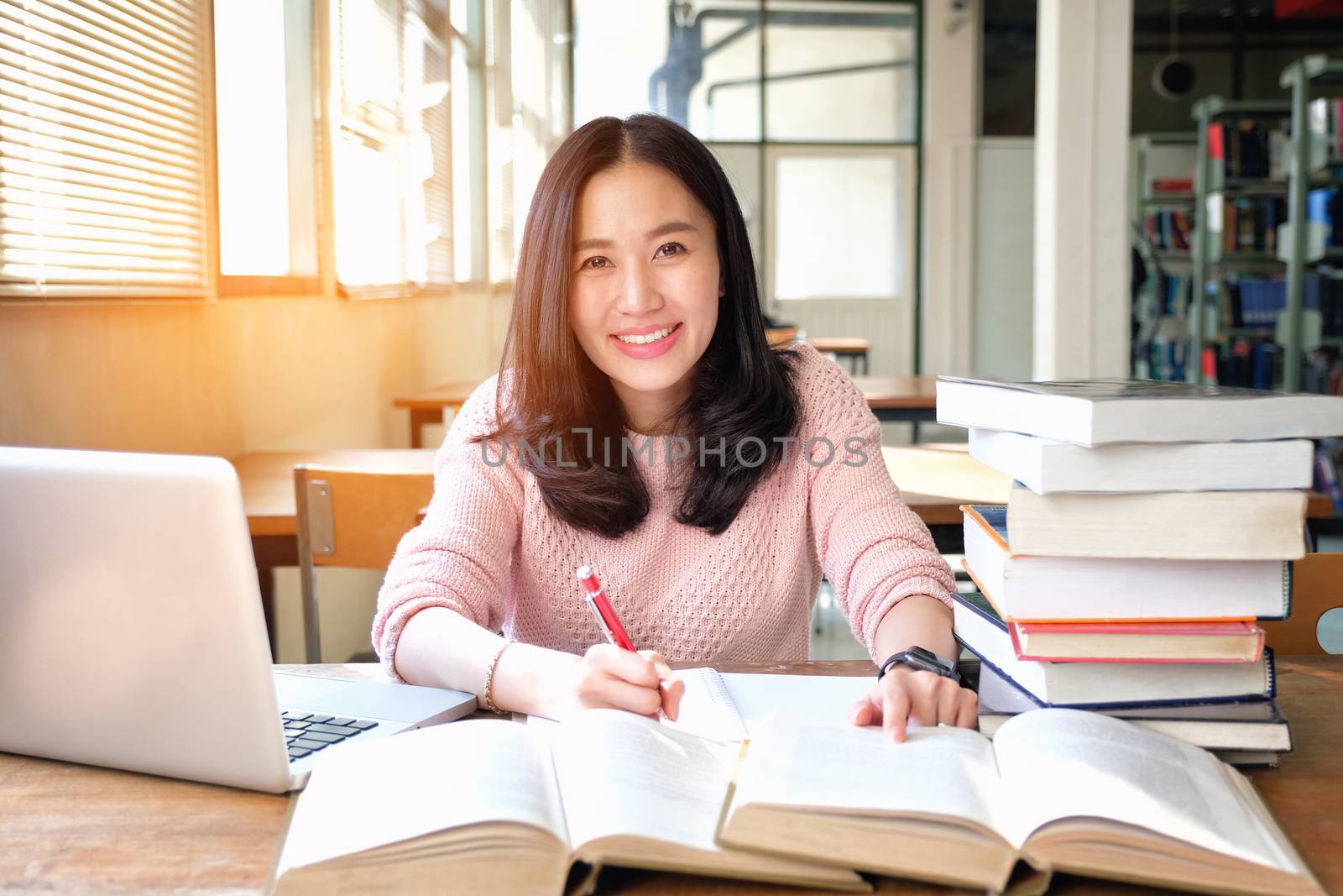 Young woman taking note and using laptop while studying in libra by Surasak