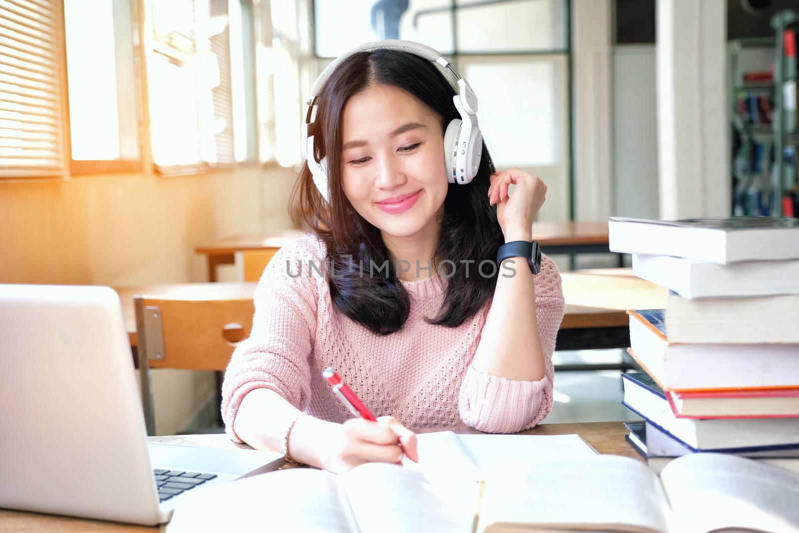 Young woman in a good mood listening to music  while studying in a library