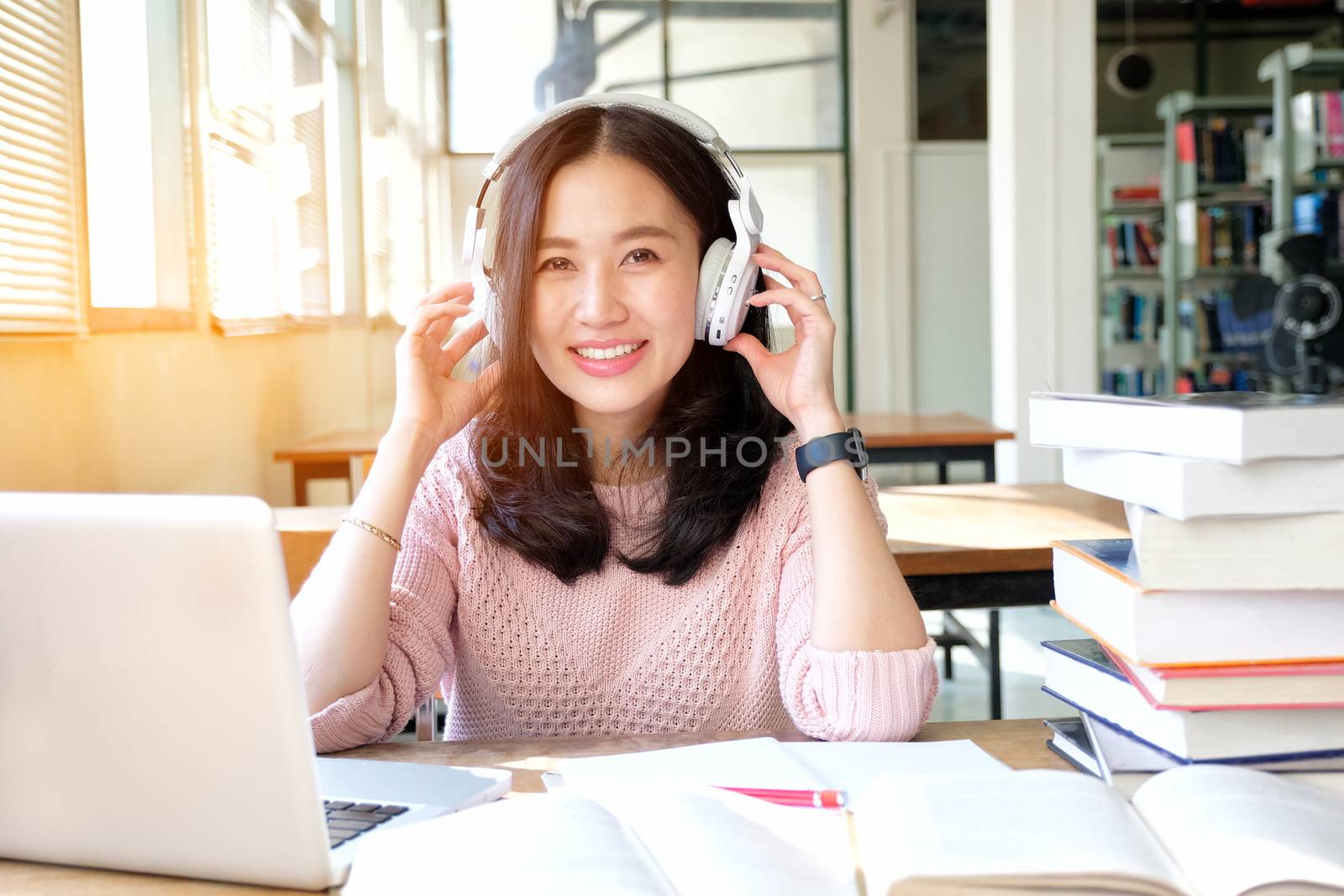 Young woman in a good mood listening to music  while studying in by Surasak