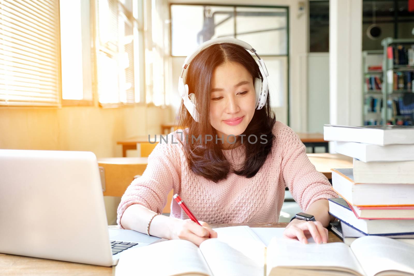 Young woman in a good mood listening to music  while studying in by Surasak