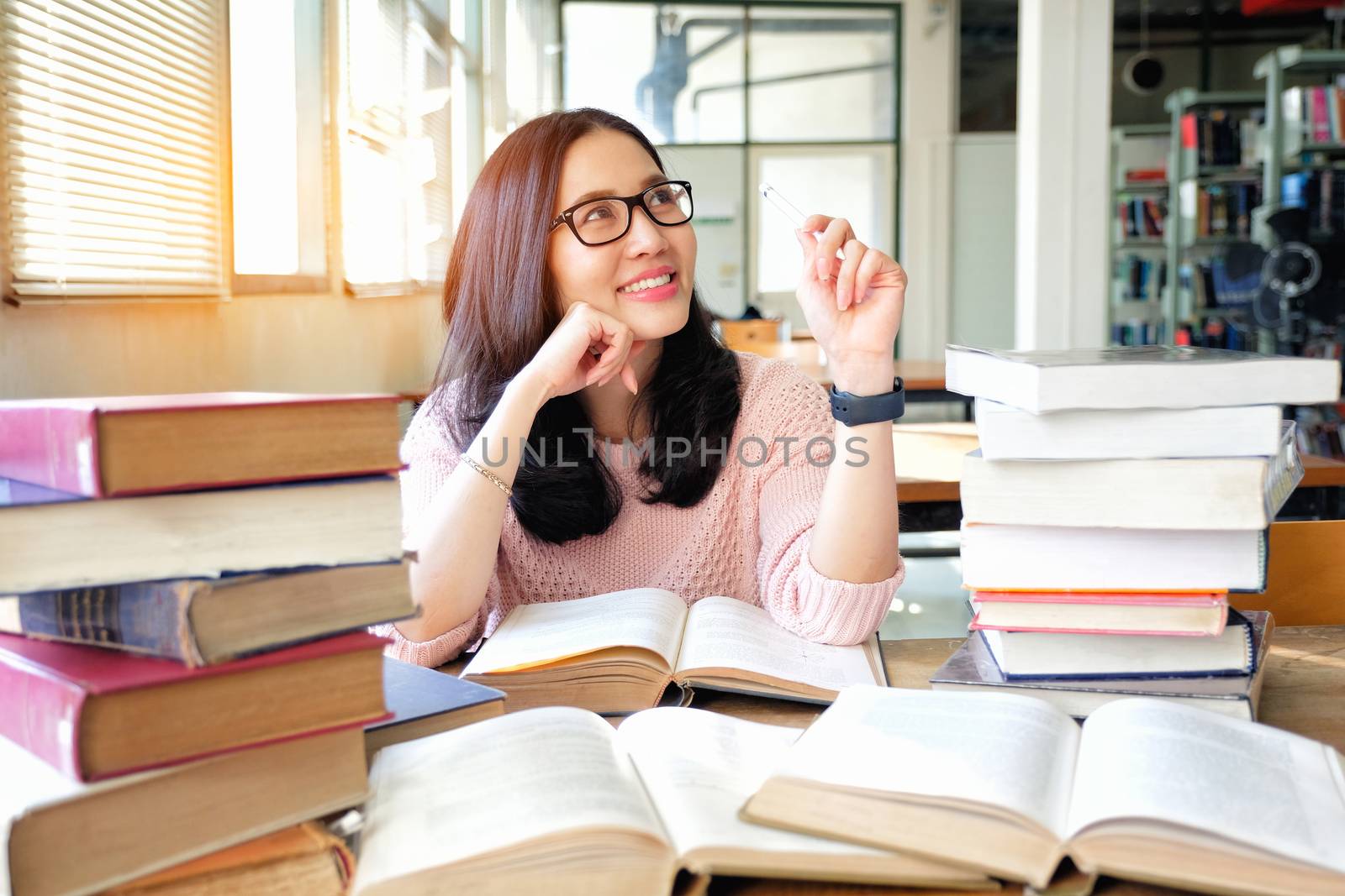 Young woman thinking while studying in library by Surasak