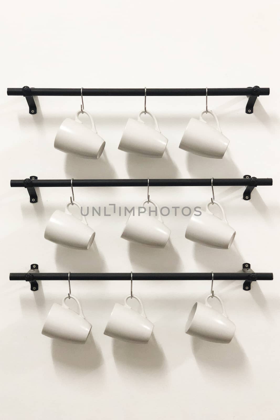 Ceramic coffee cups hanging on hooks in white wall.