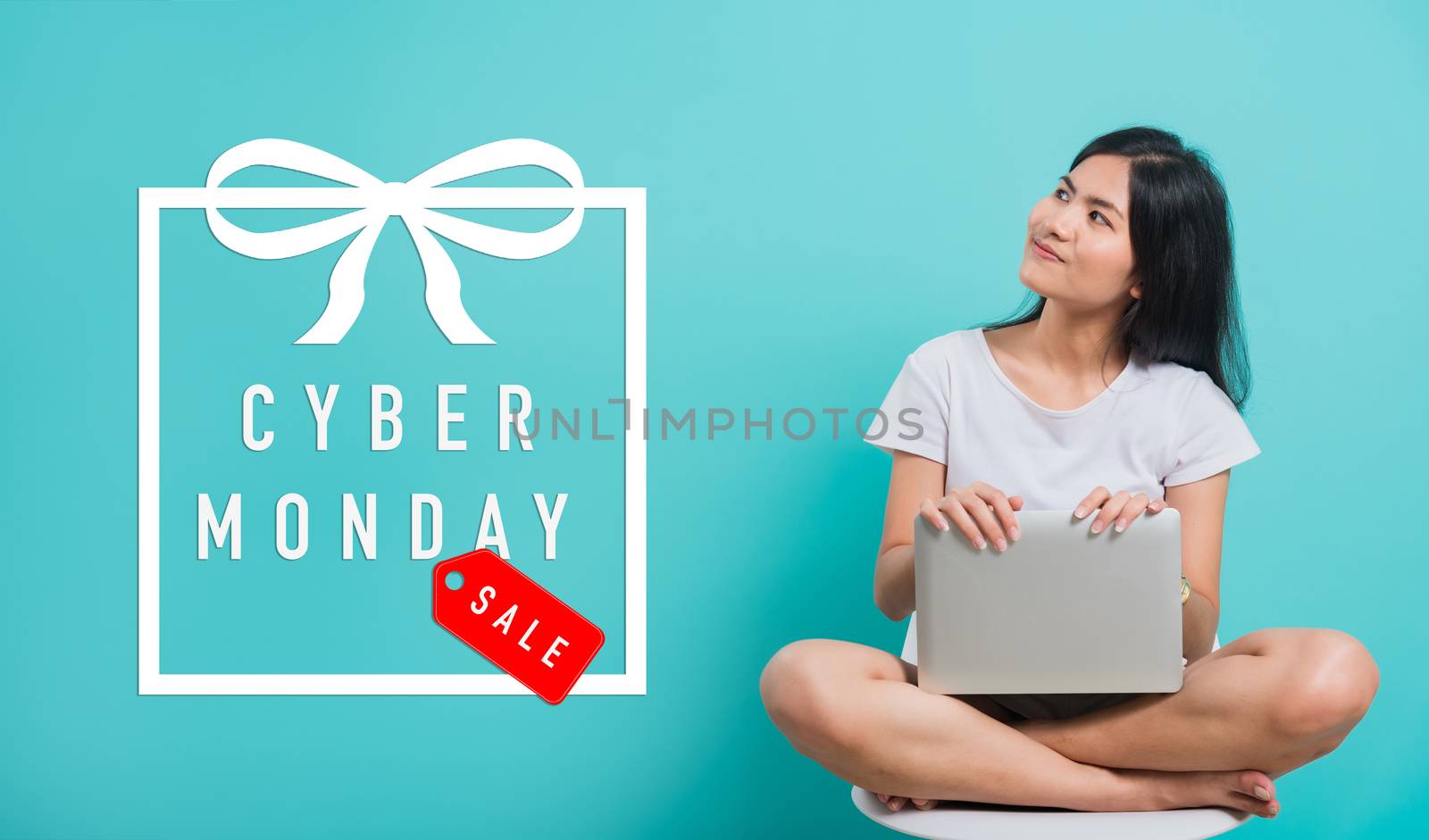Asian beautiful young woman smile she sitting on chair, She holding or using a laptop computer with Cyber Monday text on space, studio shot on blue background