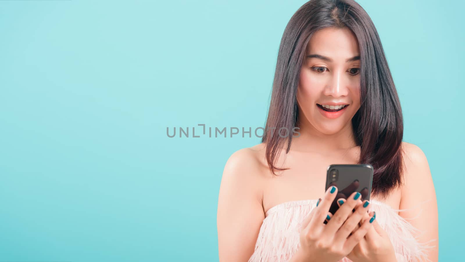 Asian happy portrait beautiful young woman standing smile her  holding smartphone or mobile phone and looking to the phone on blue background with copy space for text
