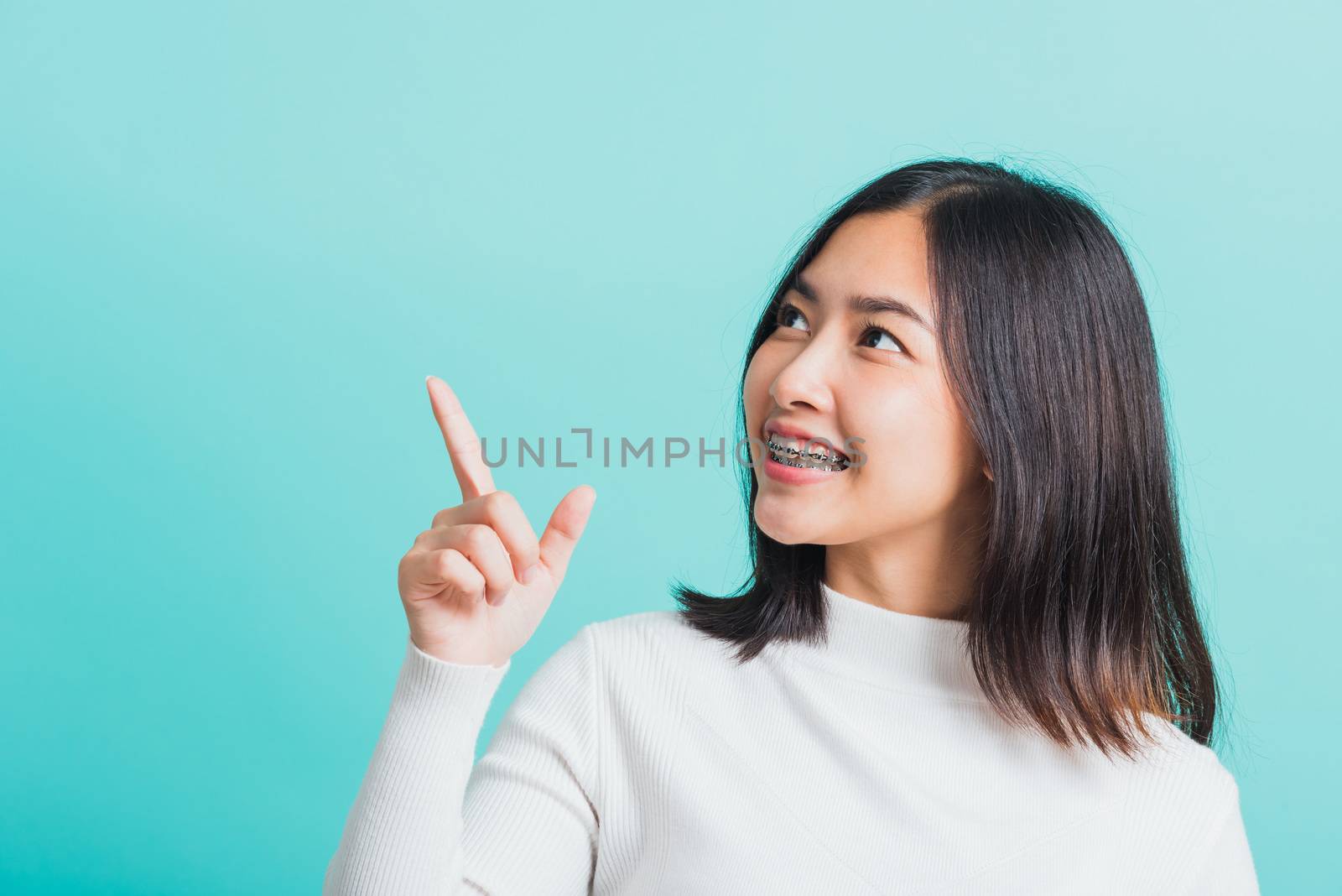 Portrait of Asian teen beautiful young woman smile have dental braces on teeth laughing point finger side away blank copy space, studio shot isolated on blue background, medicine and dentistry concept