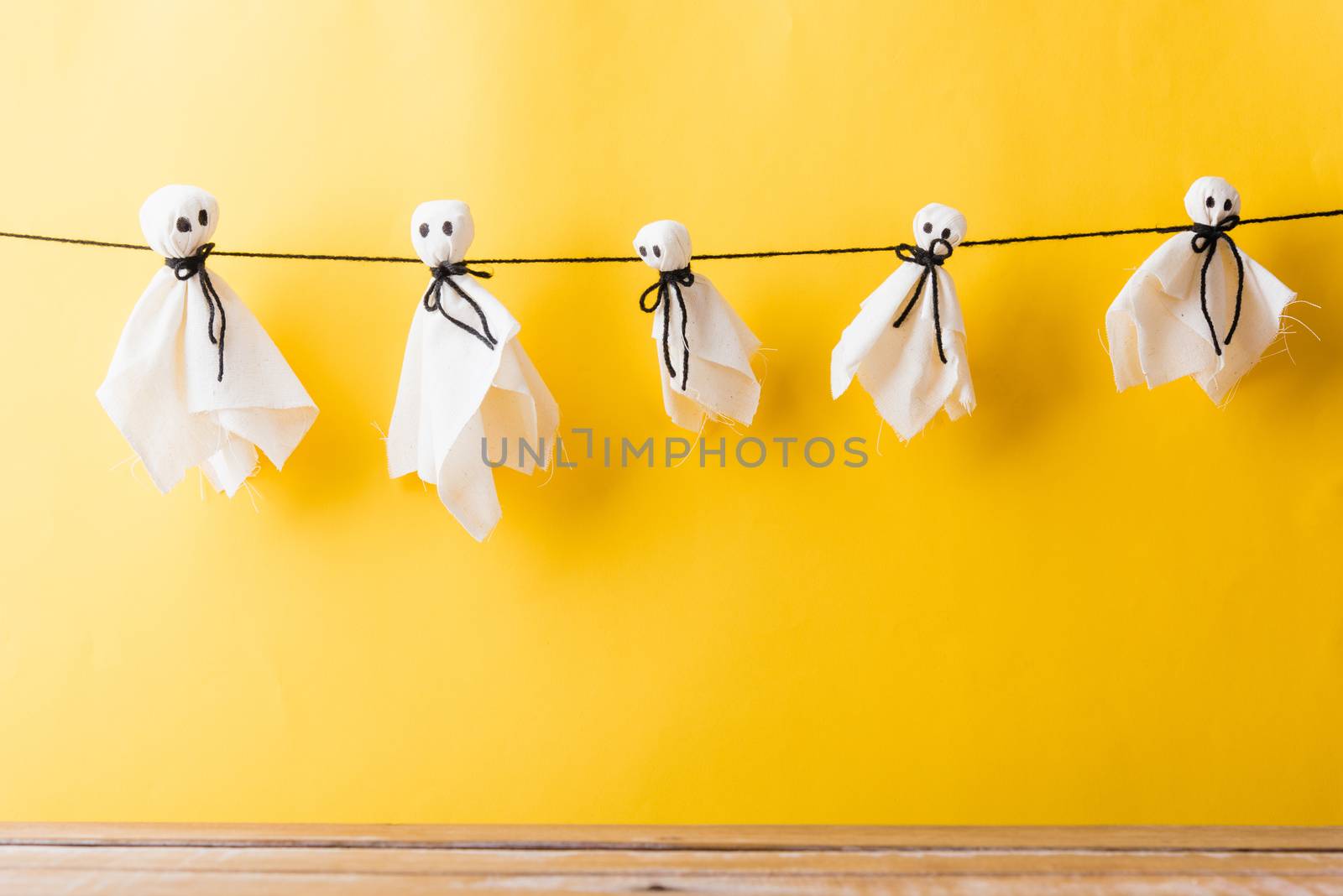 Funny Halloween day decoration party, Full body of baby cute white ghost crafts scary face hanging and wooden space, studio shot isolated on yellow background, Happy holiday DIY handicraft concept