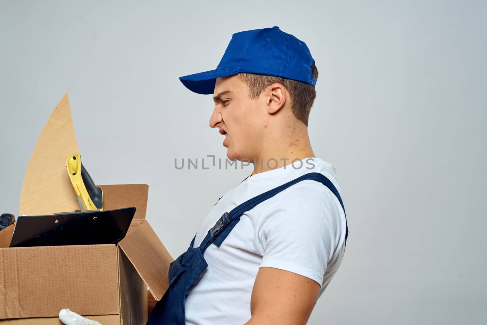 man in working uniform with a box in his hands tools loader delivery light background by SHOTPRIME