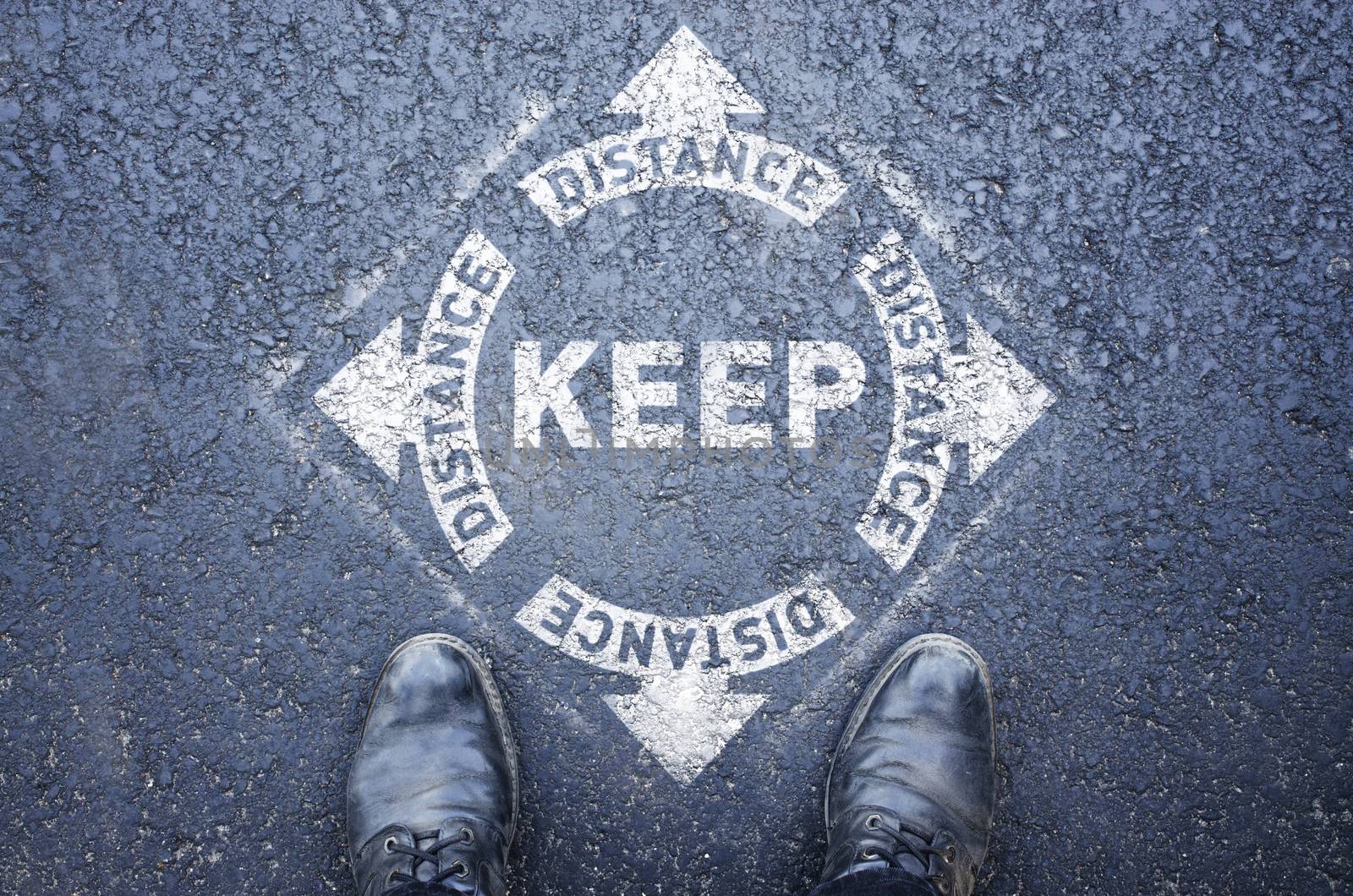 Man standing on white sign. keep distance. Sign painted on the pavement reminding users to maintain a physical distance during the COVID-19 pandemic. by mtx