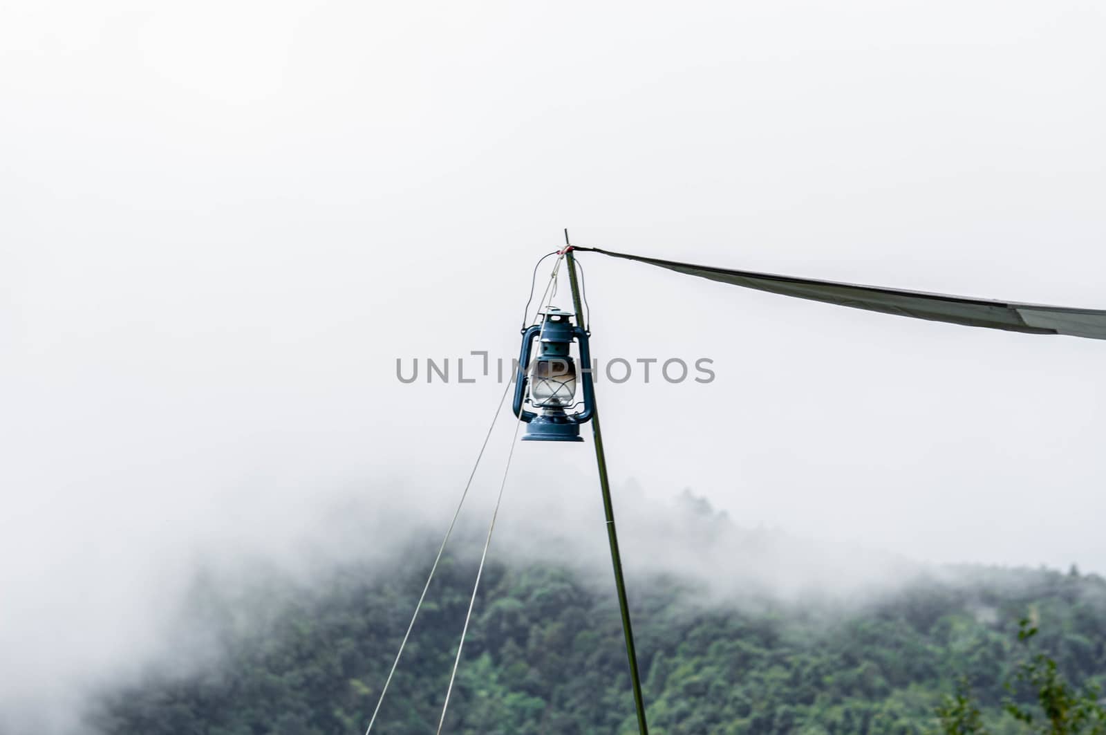 A kerosene lamp hanging on a pole in front of the tent against the background of beautiful mountain landscape and the morning mist.