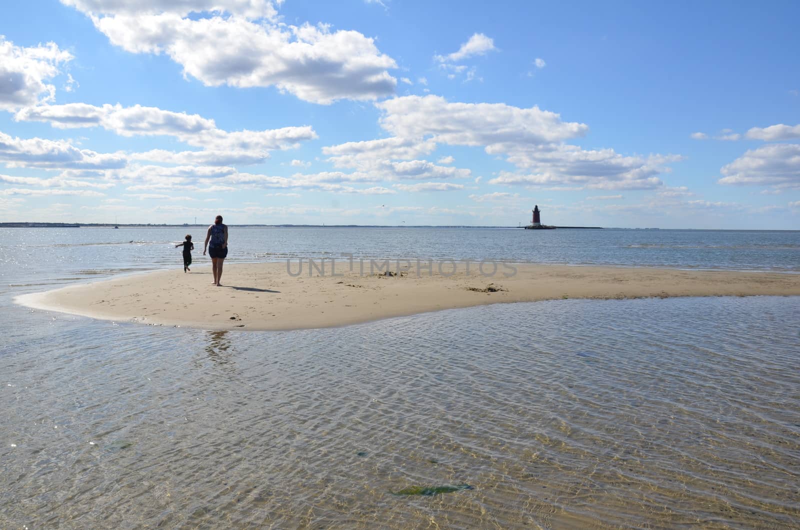 mother and child playing on beach with lighthouse by stockphotofan1